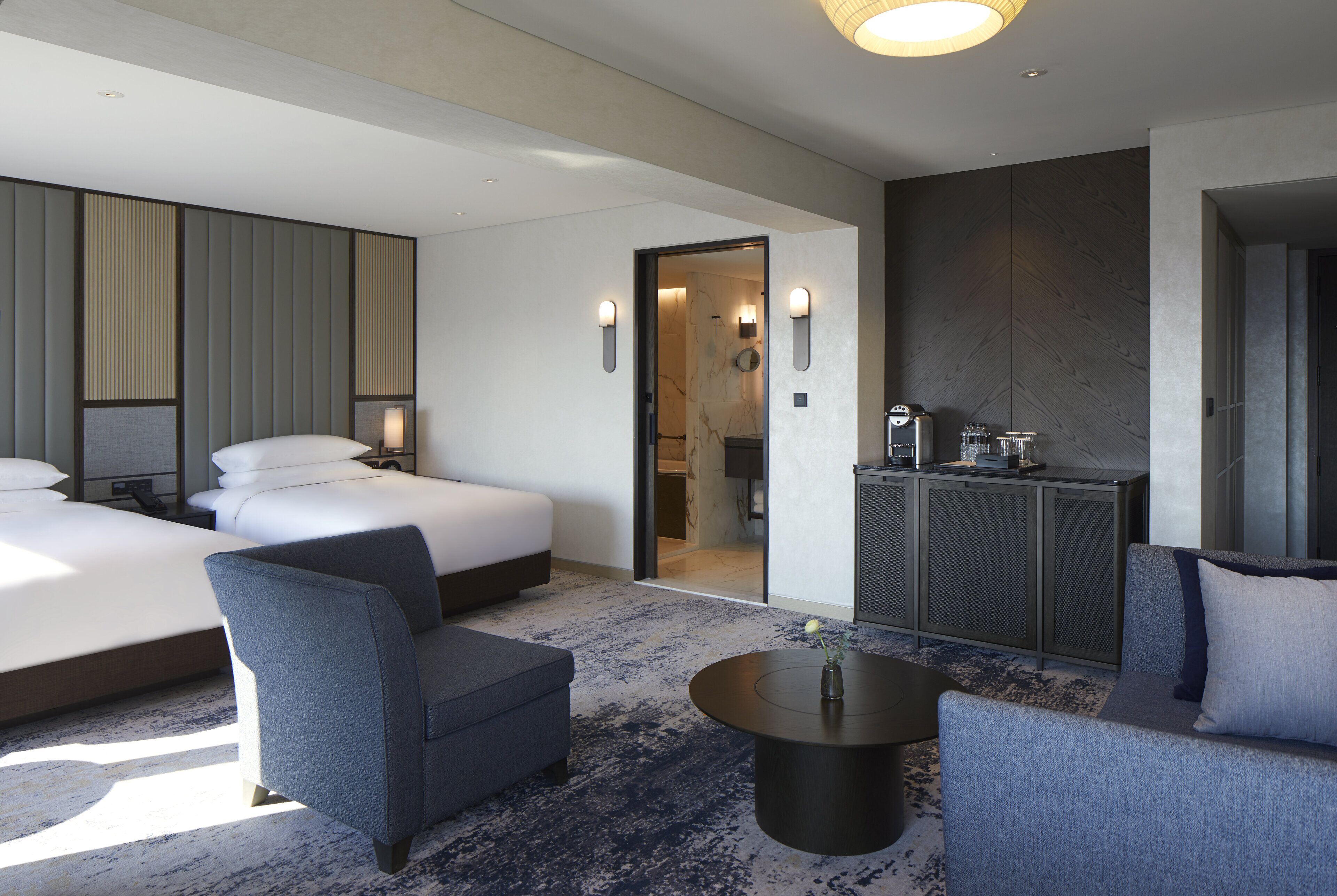 Een hotelkamer met een groot bed, twee nachtkastjes, een zithoek met een bank en fauteuils, een klein tafeltje en een badkamer zichtbaar door een geopende deur.