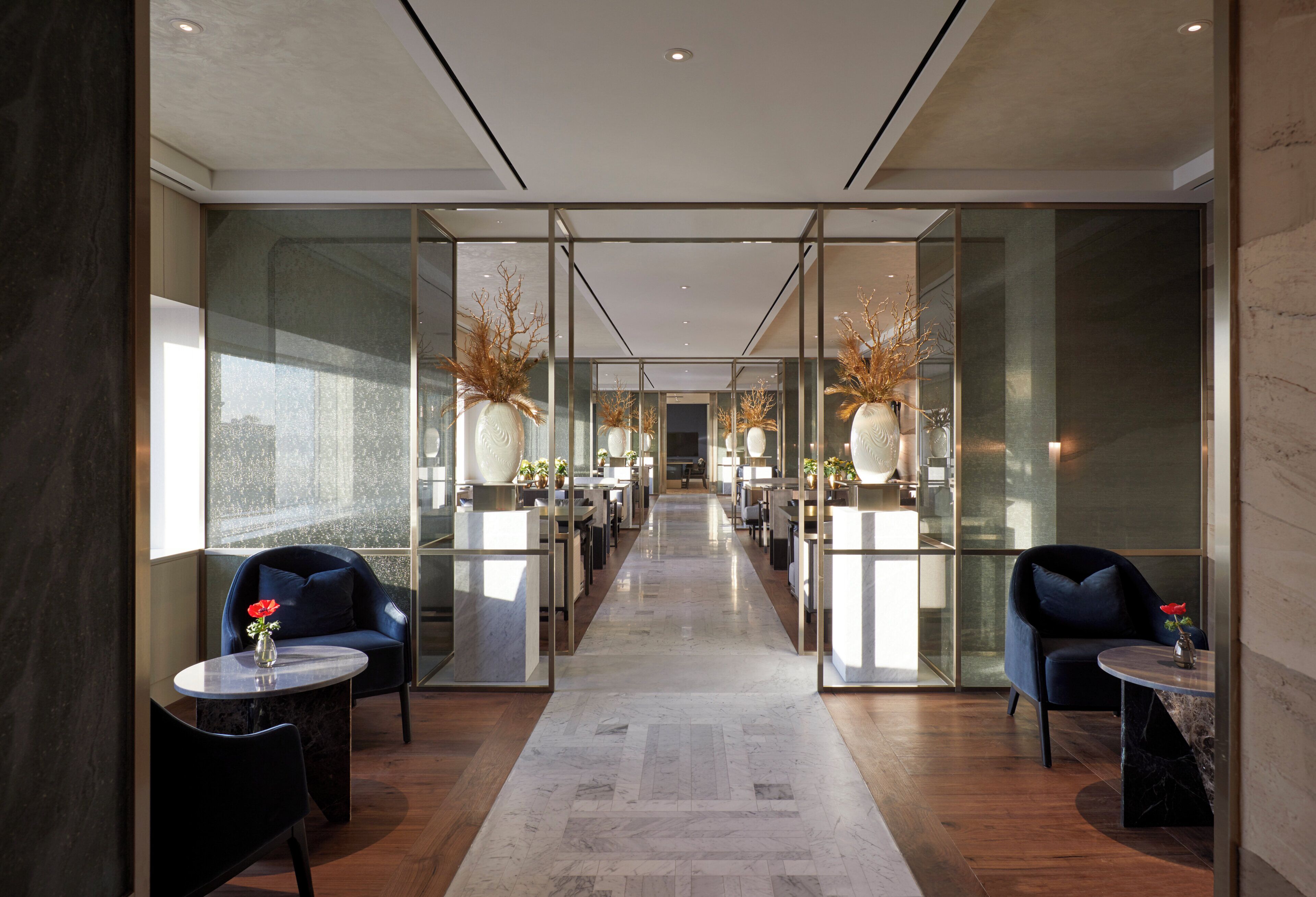 A modern hotel lobby with a central corridor, seating areas on either side, and decorative vases on tables.