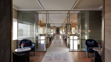 A modern hotel lobby with a central corridor, seating areas on either side, and decorative vases on tables.