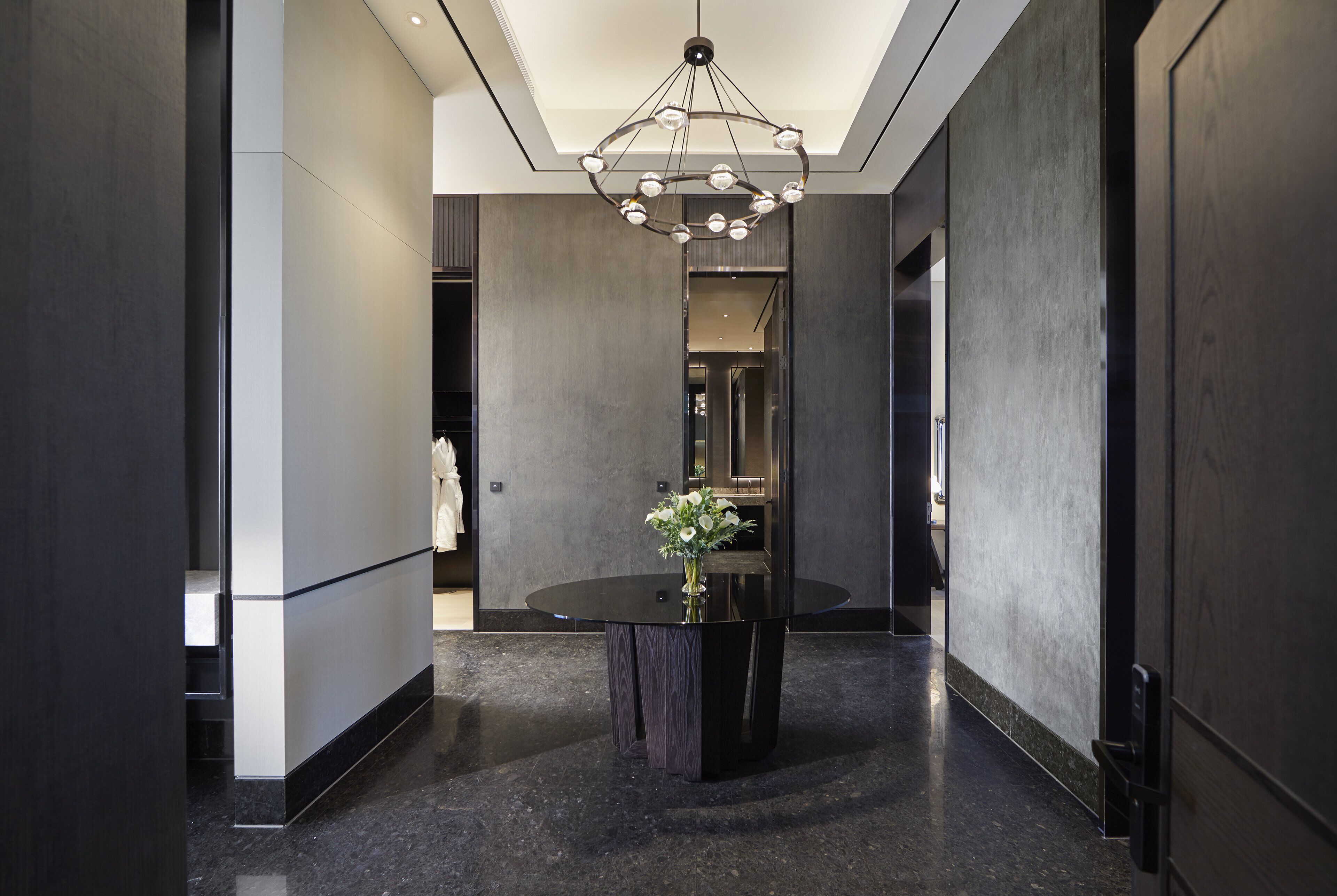 Un hall d’entrée moderne avec une table ronde, un lustre et un vase rempli de fleurs.