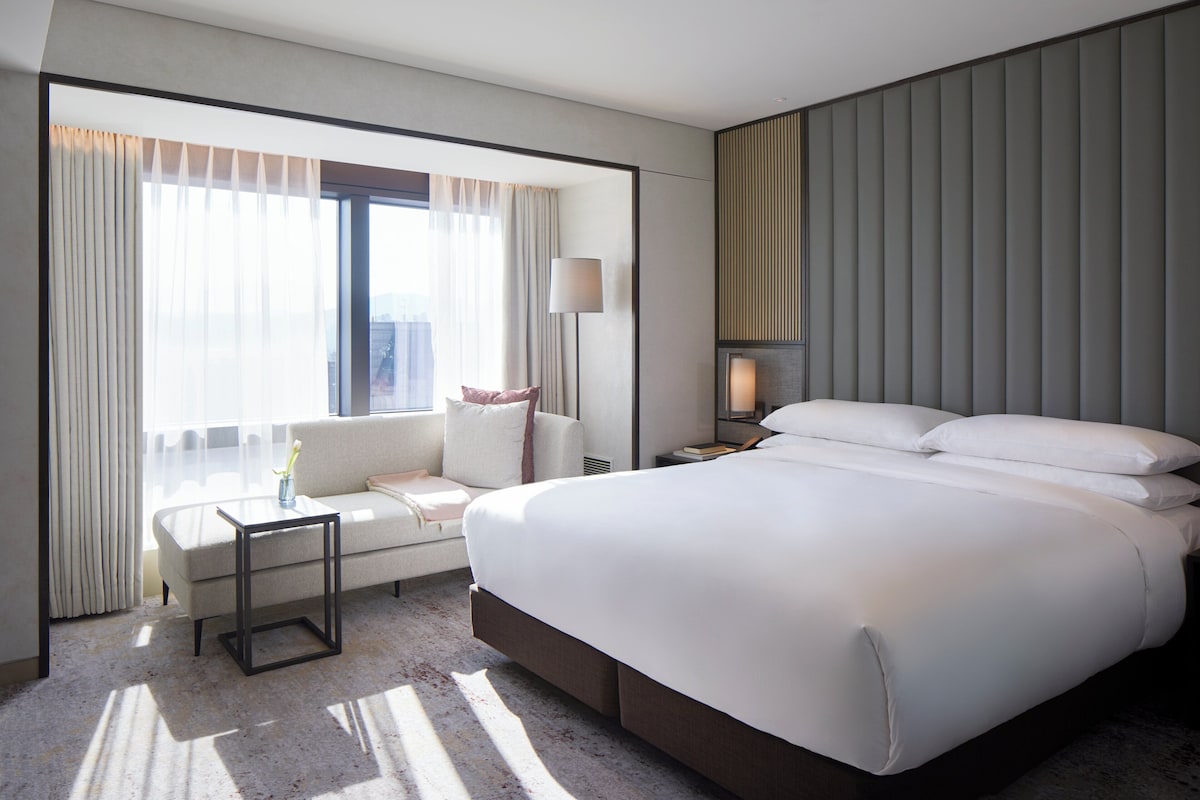 A modern hotel room with a large bed, a sofa, a small table, and a lamp.