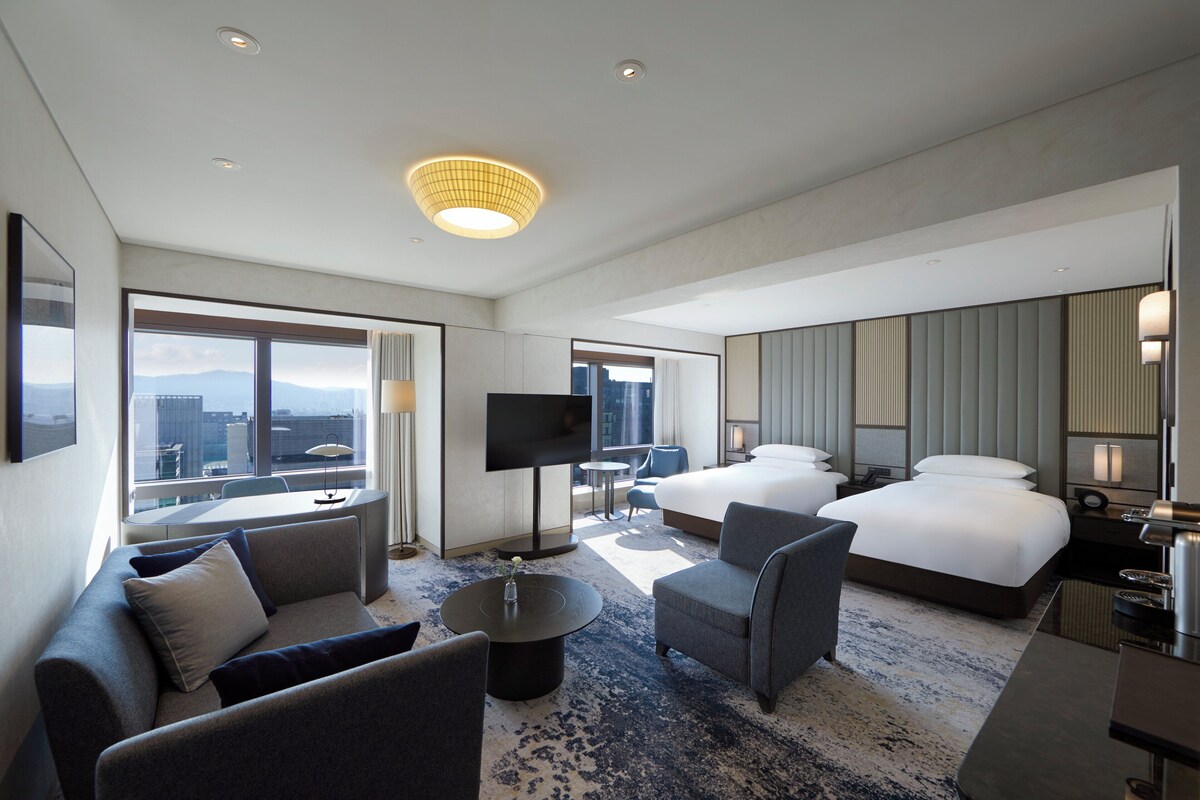 A modern hotel room with a large bed, a sofa, a coffee table, and a TV.