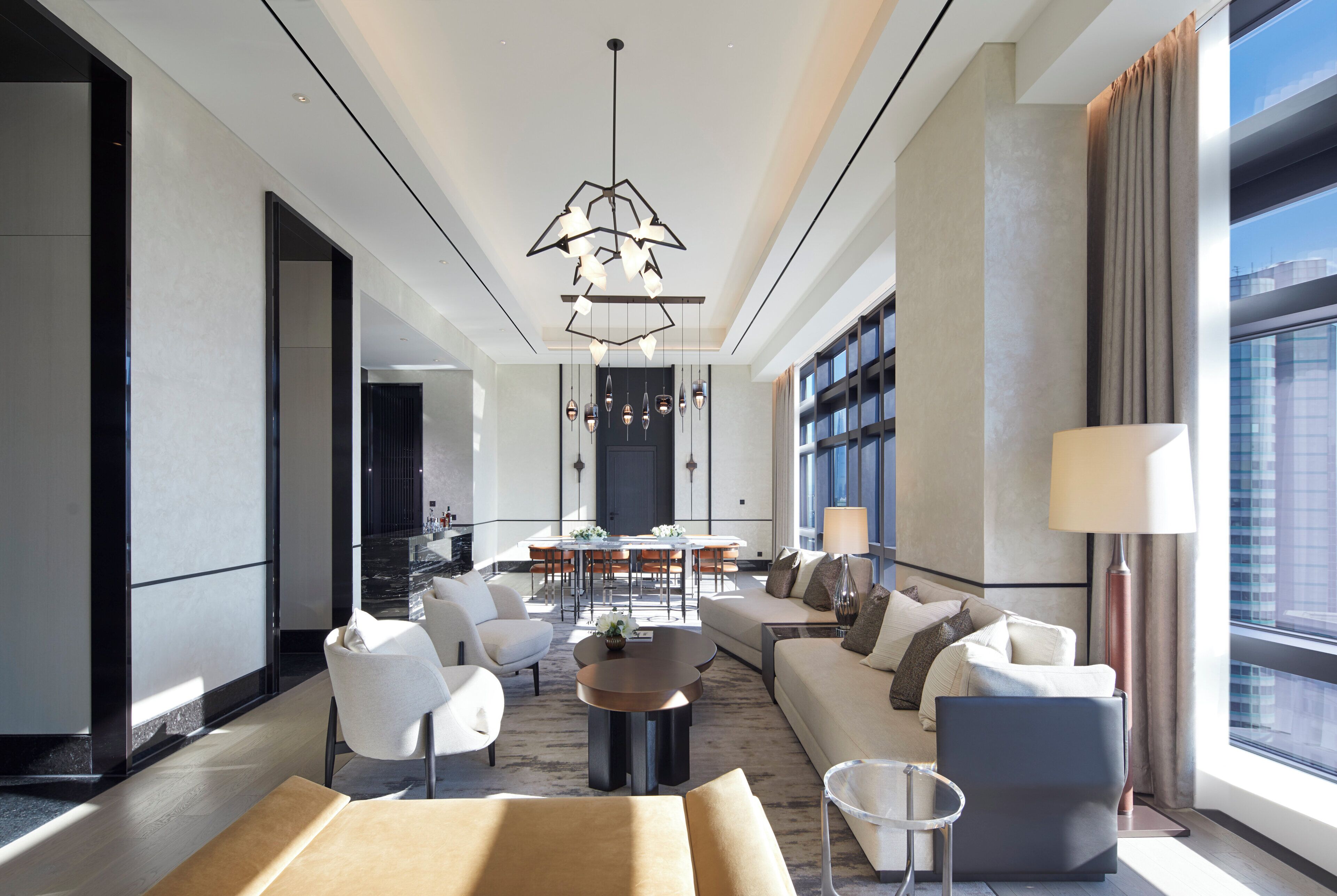 A modern hotel lobby with a central seating area, a dining table, and a large window offering a view of the city.