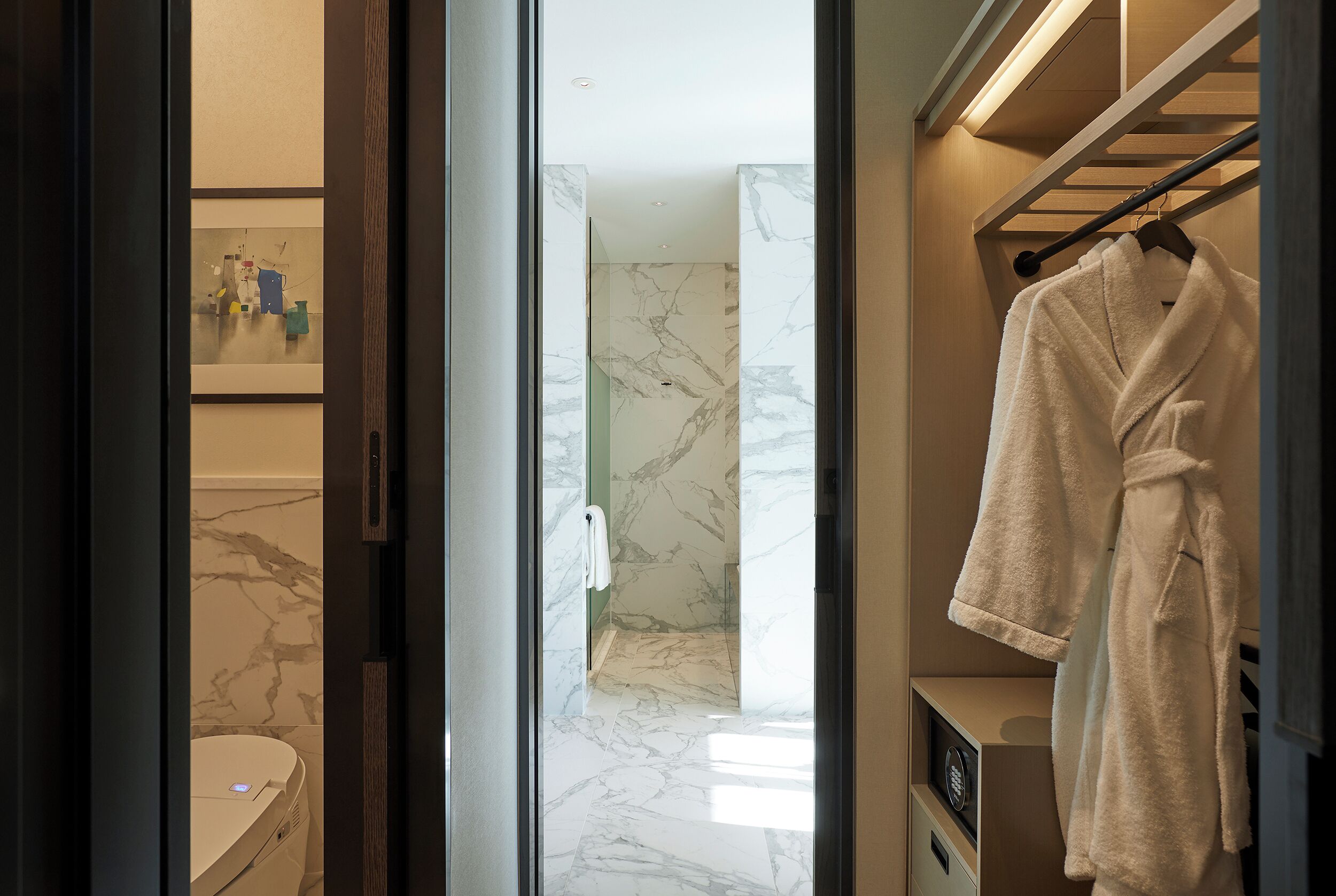 A modern bathroom with a marble floor, a white toilet, and a towel rack with a bathrobe.