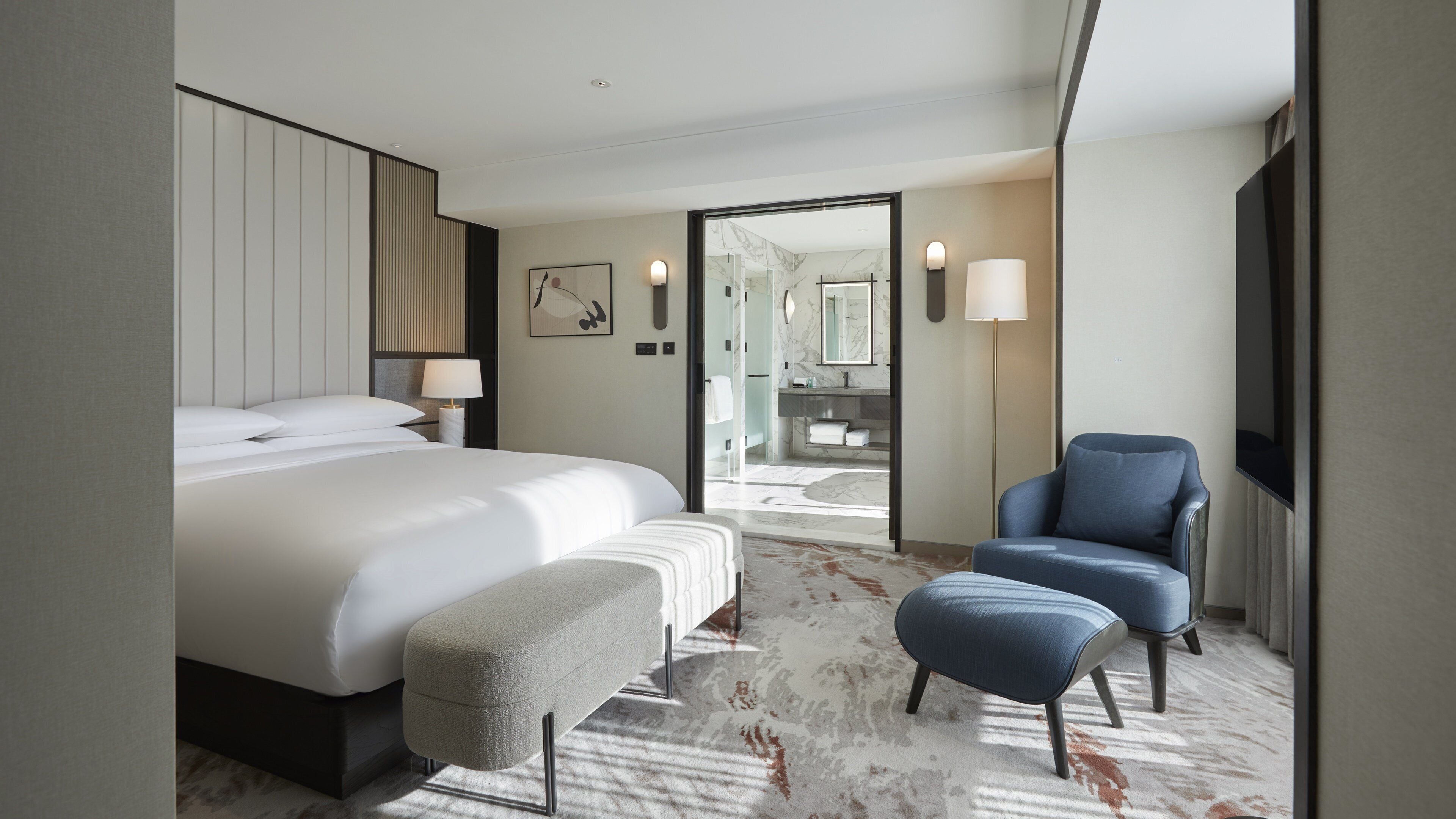 A modern hotel room with a large bed, a seating area, a bathroom with a marble vanity, and a flat-screen TV.