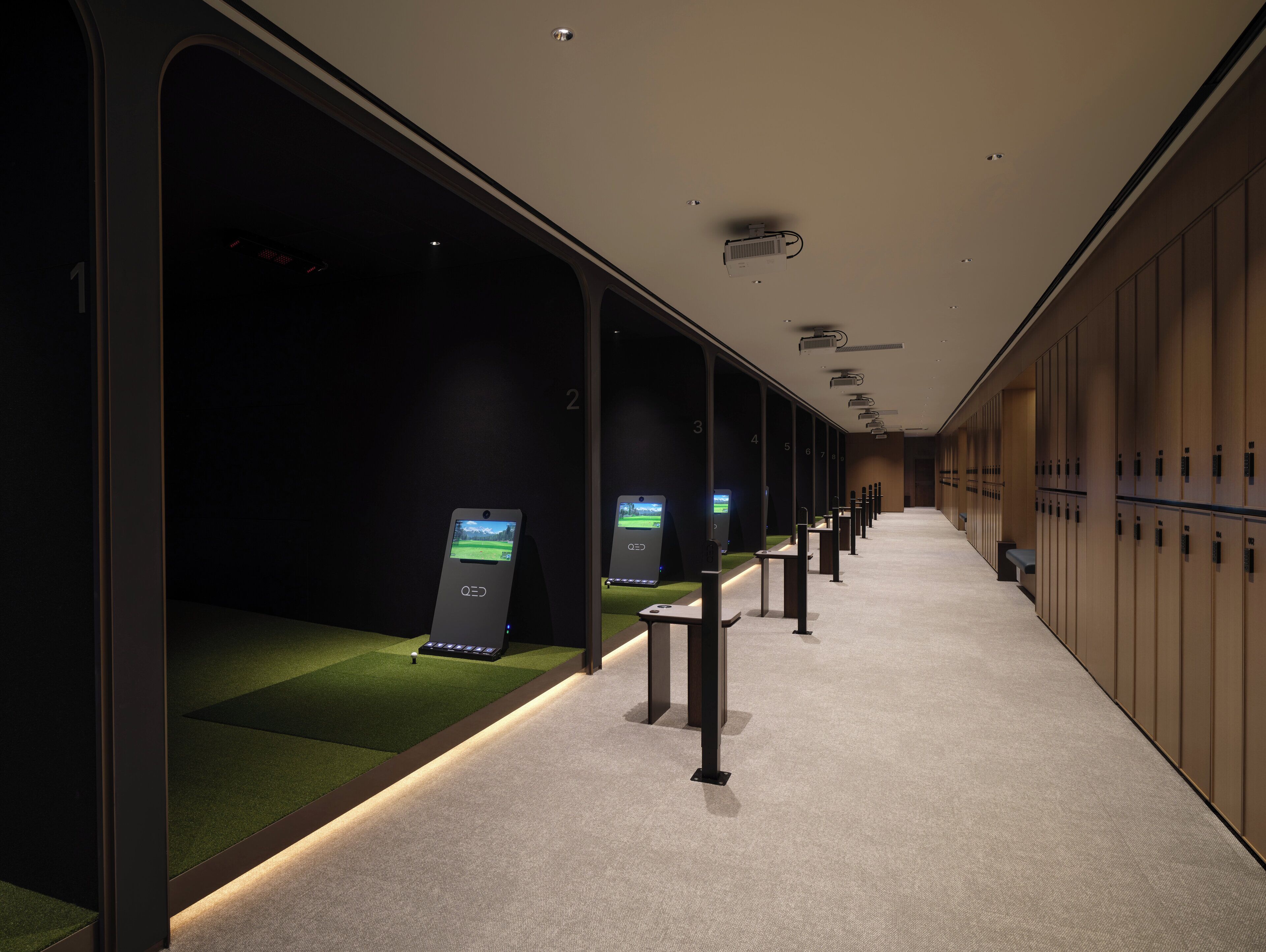 A hotel corridor with lockers, a reception area, and a green carpeted section with a digital kiosk.