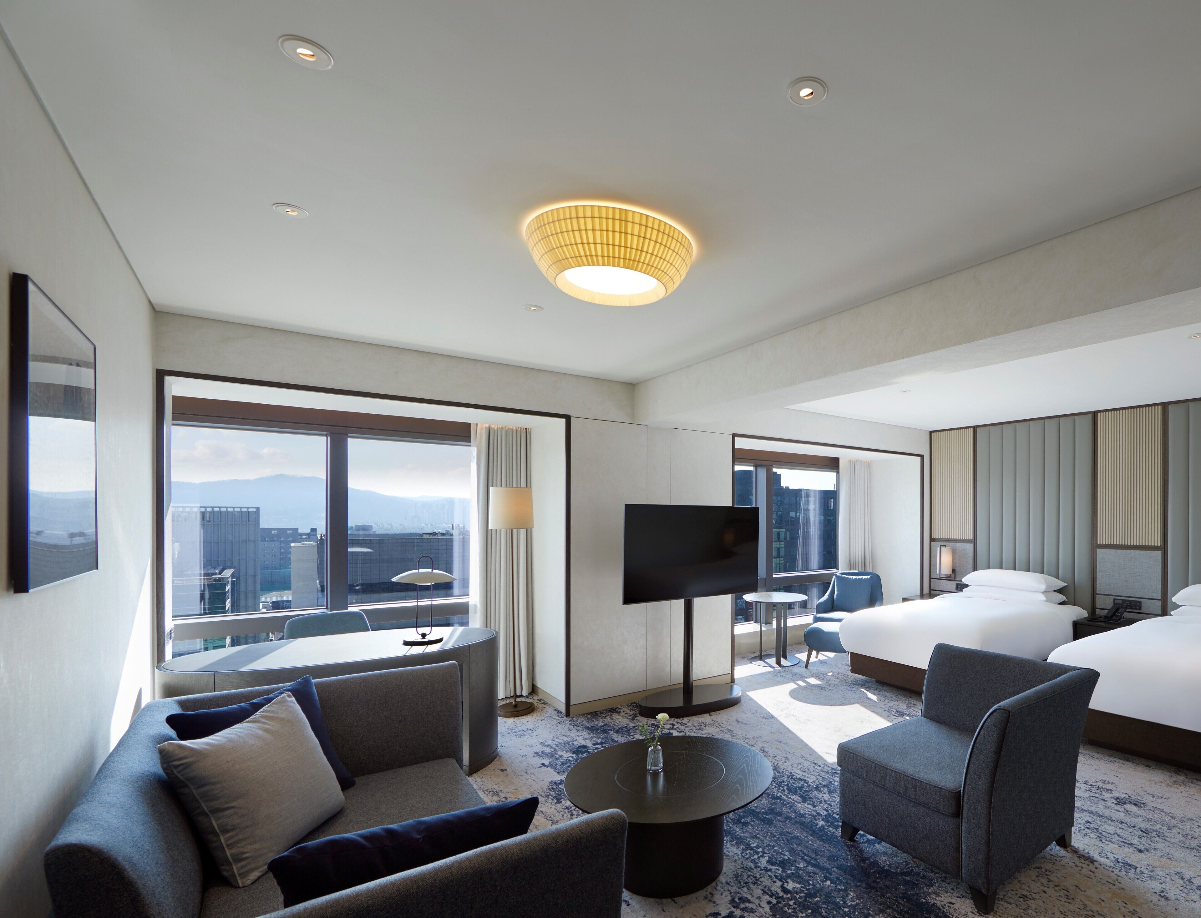 A modern hotel room with a large bed, a sofa, a coffee table, and a TV.