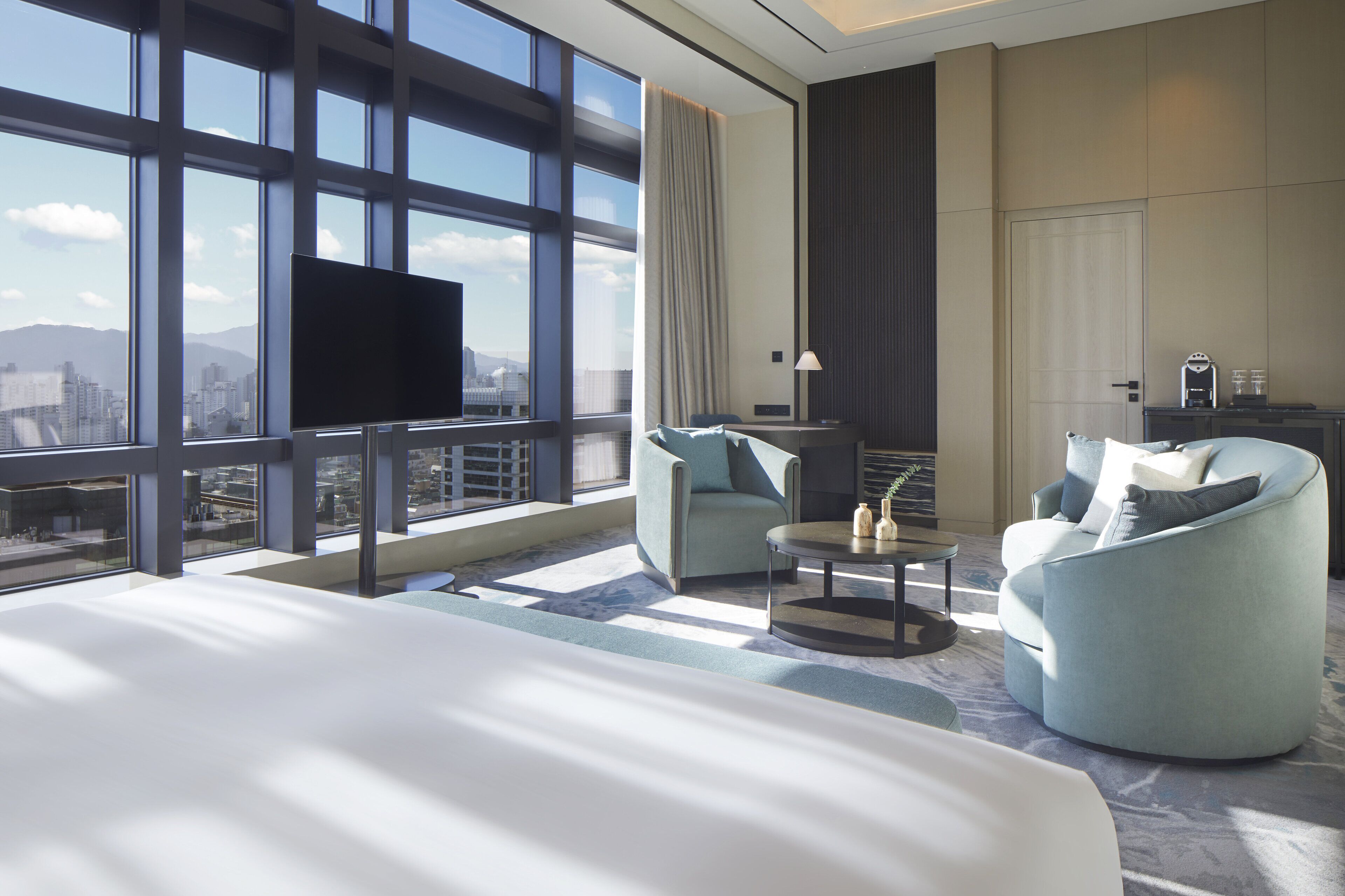 Une chambre d’hôtel moderne avec un grand lit, deux fauteuils, une petite table et un téléviseur.
