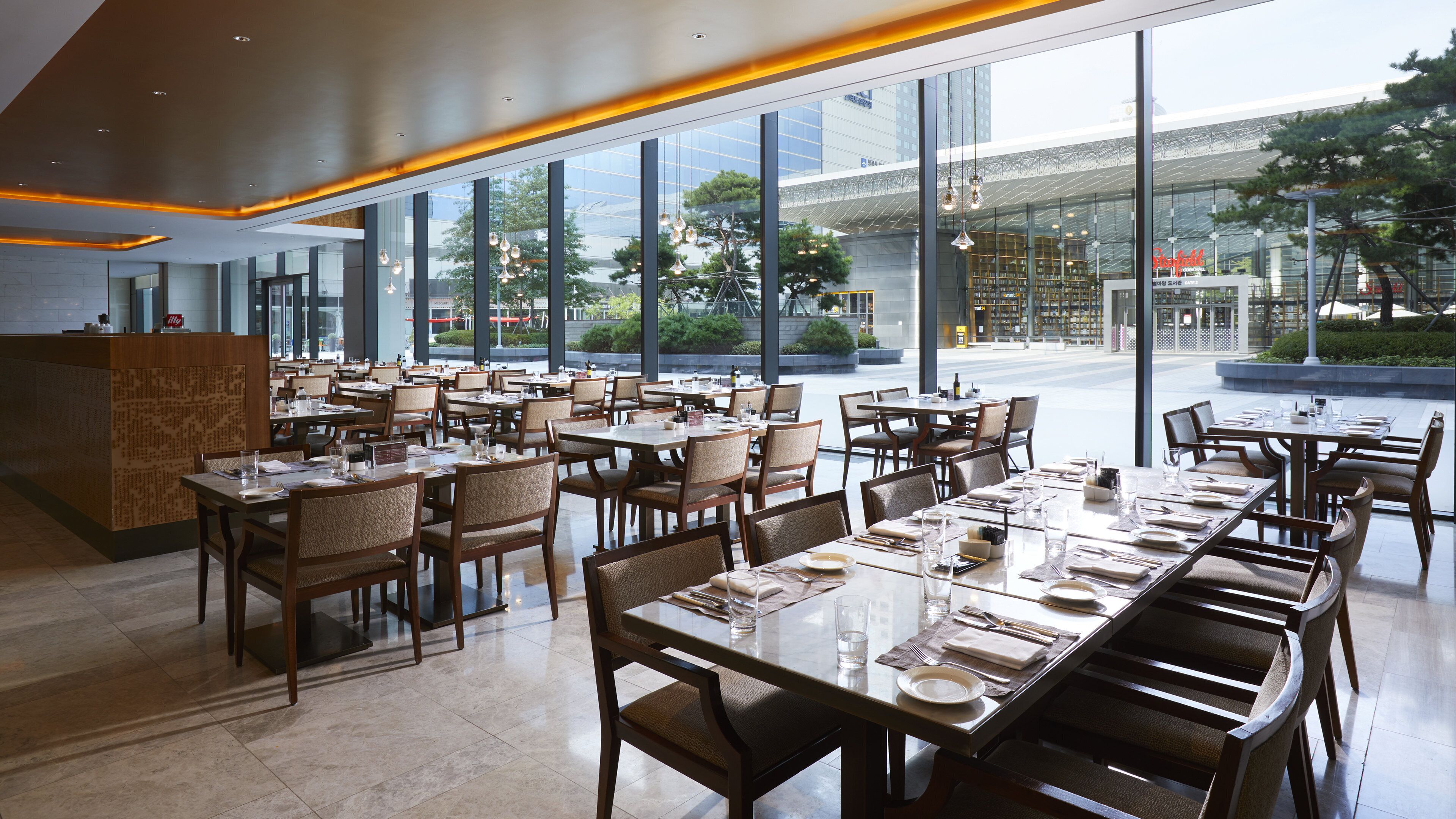 A modern restaurant with a long dining area, large windows, and a view of the outside.