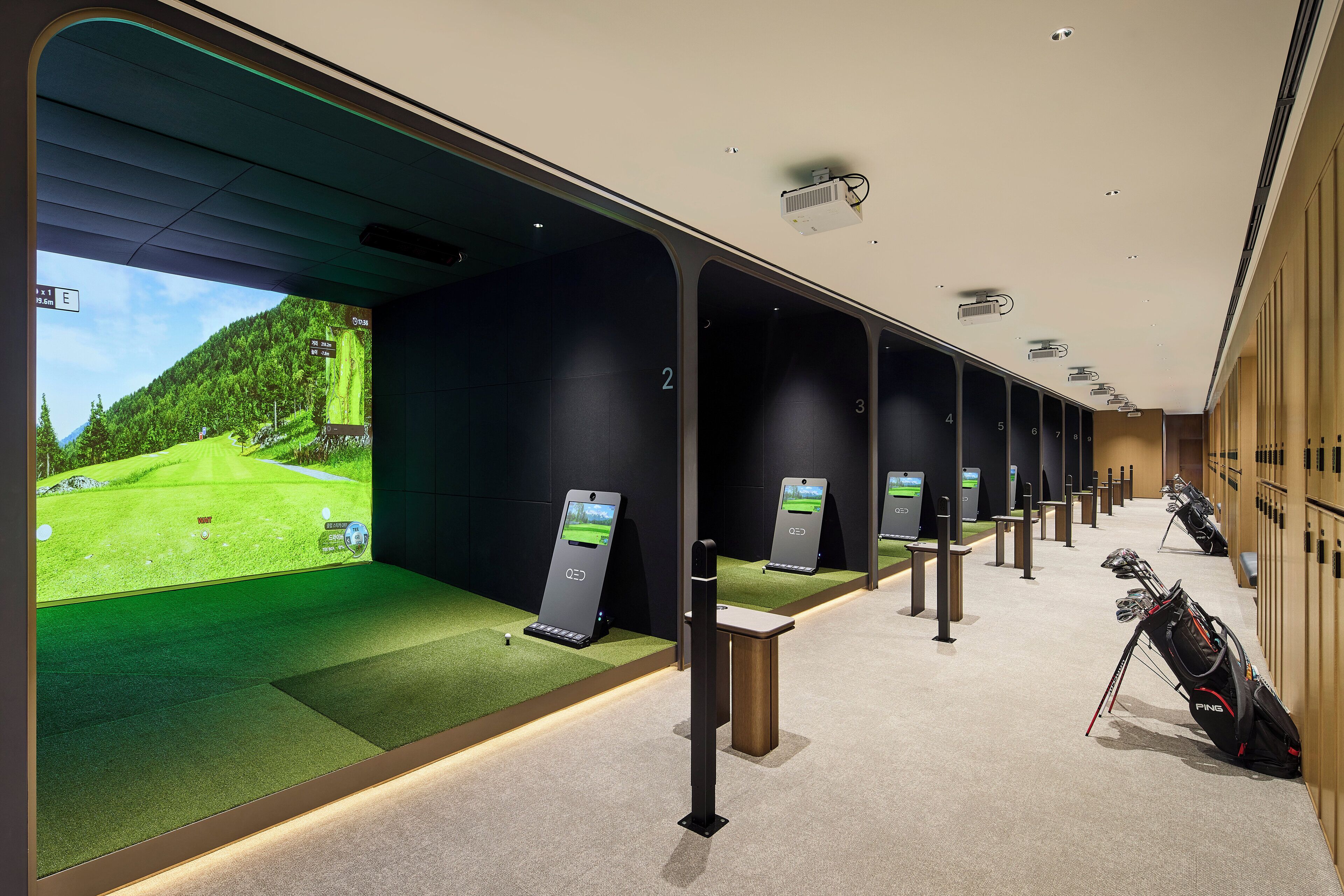 Un espacio moderno para simulación de golf en interiores, con múltiples pantallas que muestran campos de golf, taquillas numeradas y bolsas de golf.