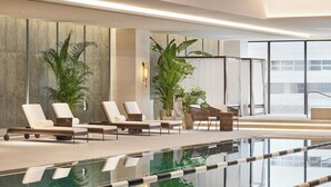 Un área de piscina interior moderna con sillones de descanso, plantas en macetas y una piscina cristalina con separadores de carril.