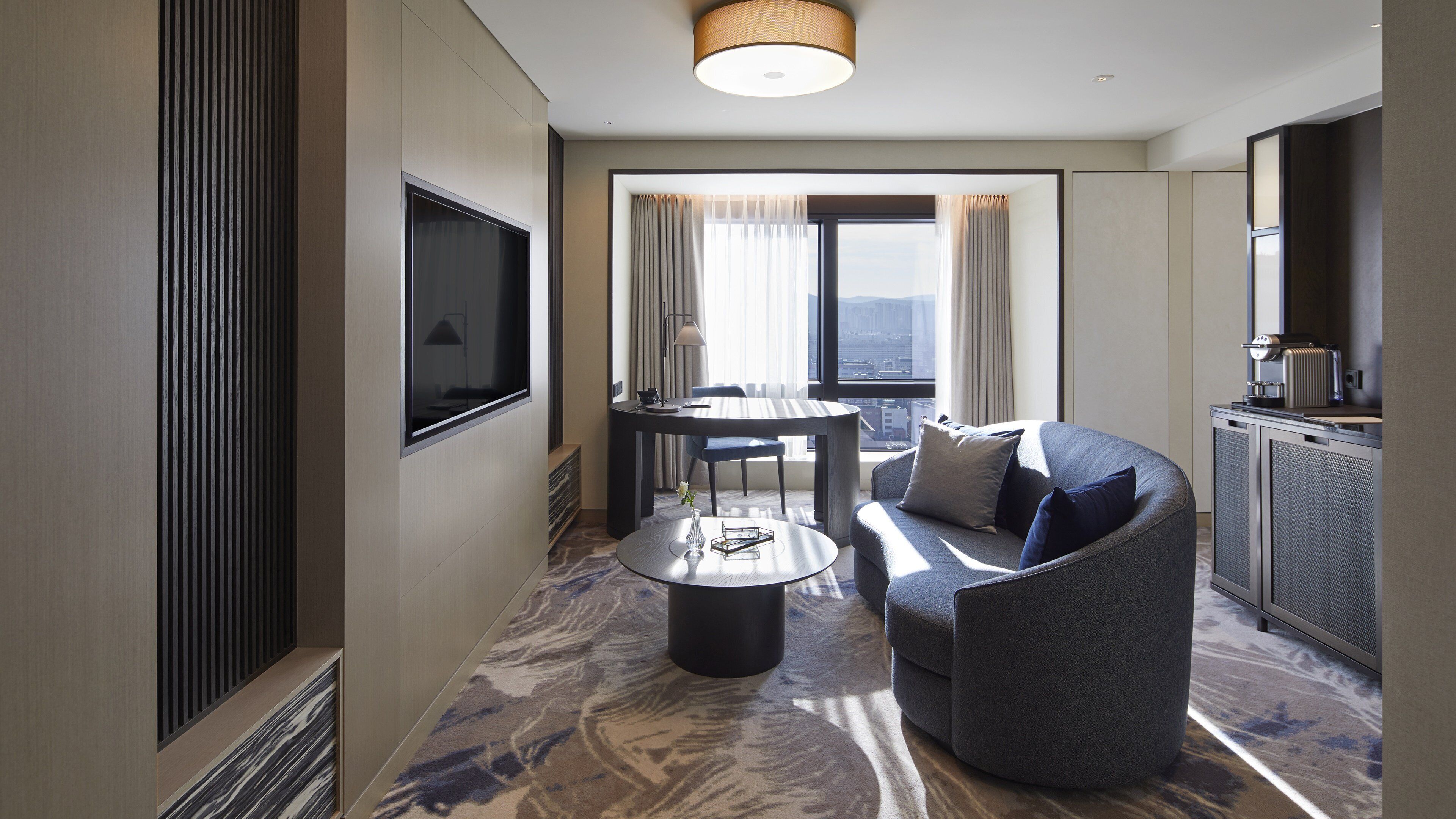Une chambre d’hôtel moderne équipée d’un canapé, d’une table à manger et d’un téléviseur fixé au mur.