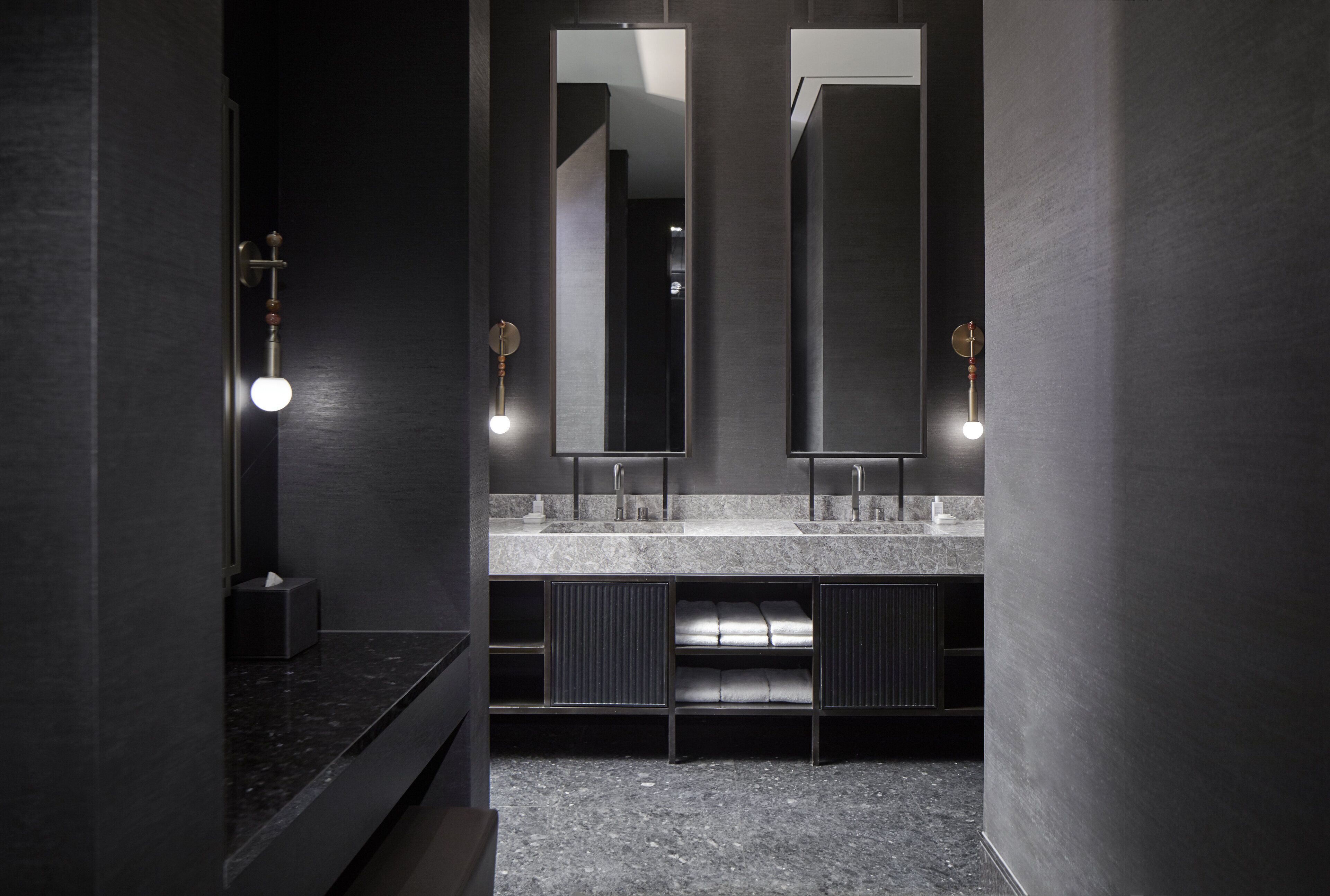 A modern bathroom with dark walls, two mirrors, a marble countertop, and built-in shelves.