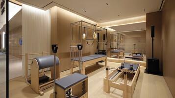 A modern, well-lit room with exercise equipment, including Pilates reformers and a bench, and a large mirror reflecting the space.
