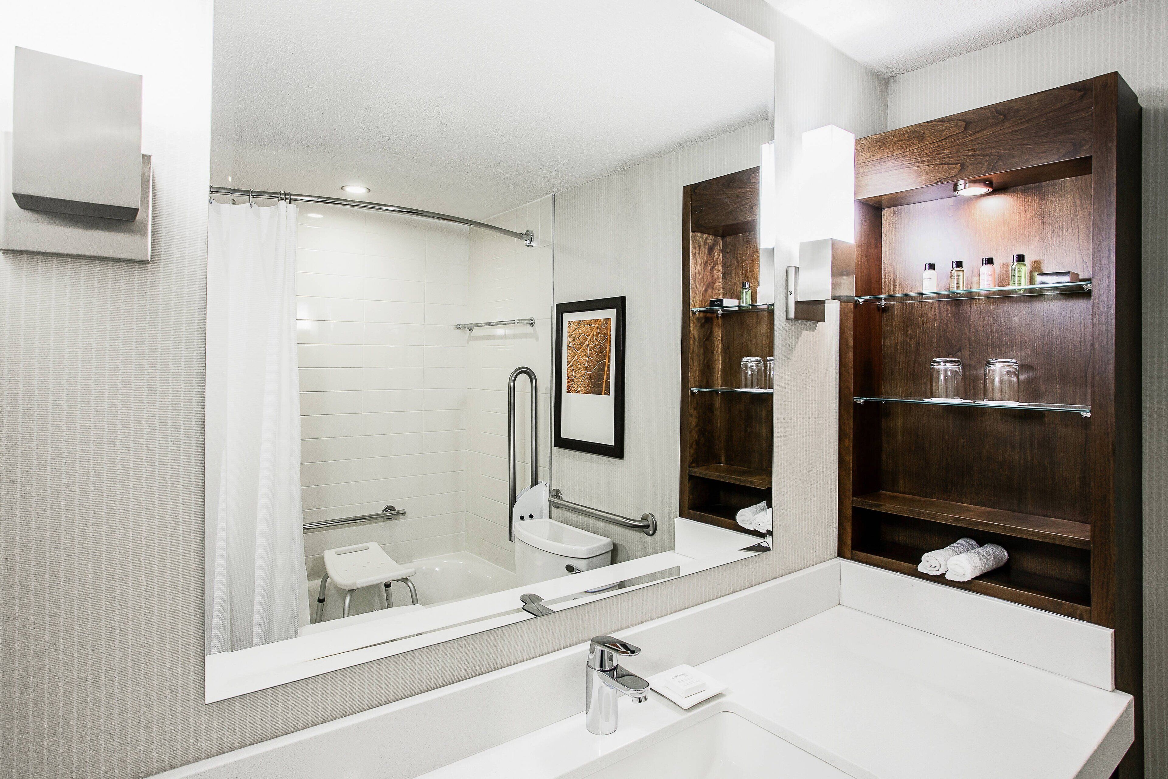 Un baño moderno con un espejo grande, un lavabo blanco y un tocador de madera con estantes.