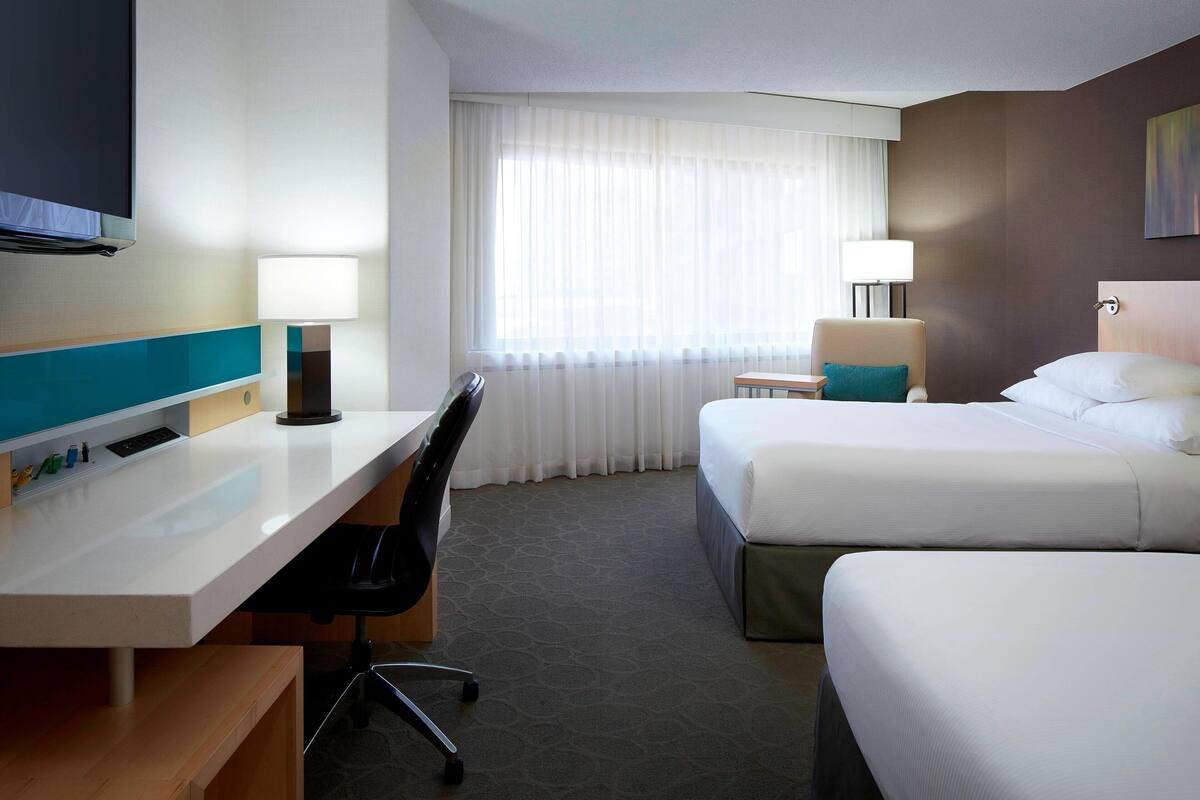 A hotel room with a desk, two beds, a TV, and a window with curtains.