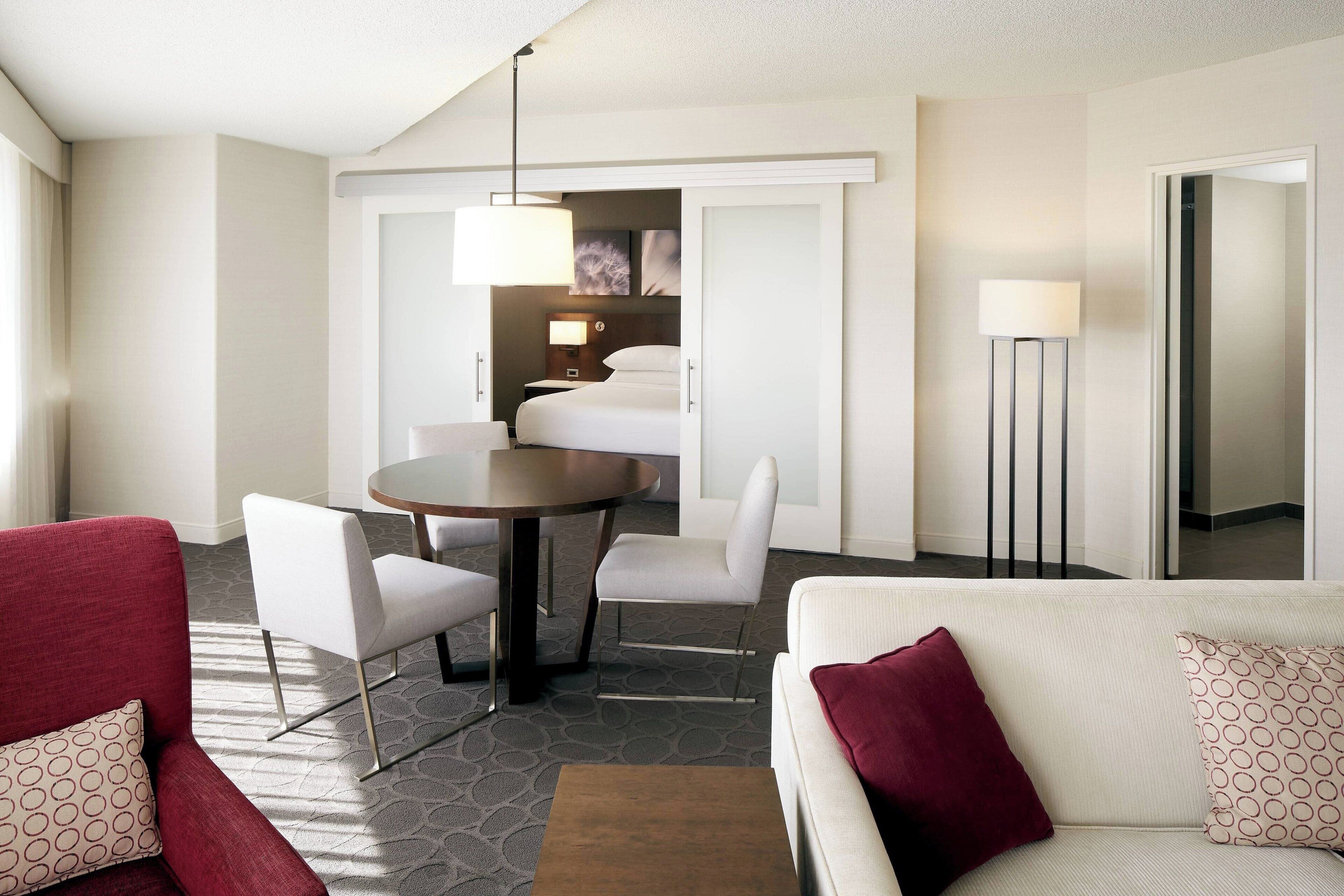 A hotel room with a dining area, a white sofa with patterned cushions, and a red armchair.