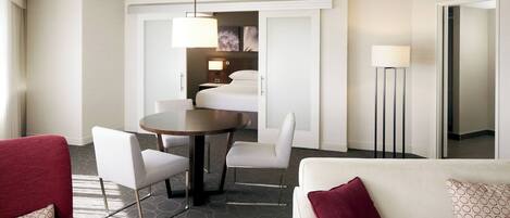 A hotel room with a dining area, a white sofa with patterned cushions, and a red armchair.
