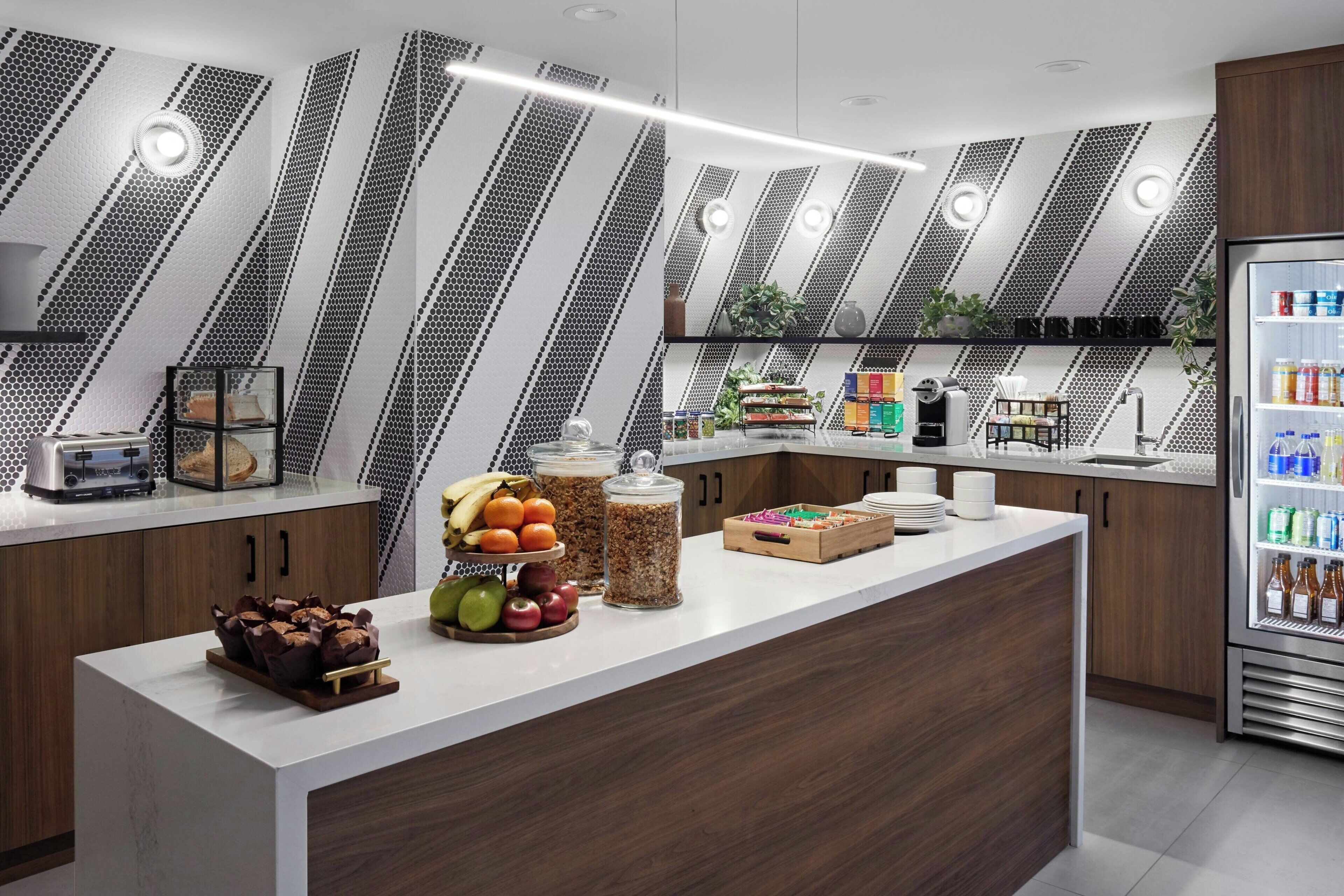 A modern kitchen with a white countertop, wooden cabinets, and a built-in refrigerator. There are various food items and kitchen appliances on the counter.