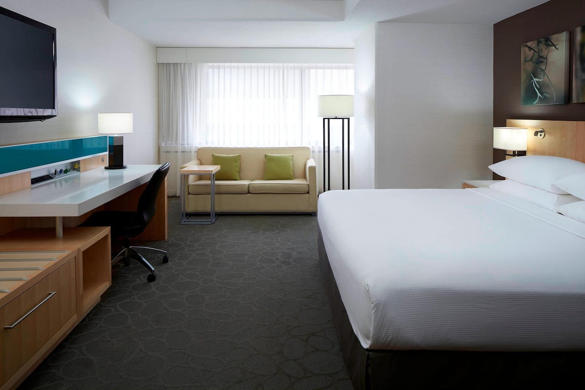 A hotel room with a bed, a desk, a chair, a sofa, a TV, and a lamp.