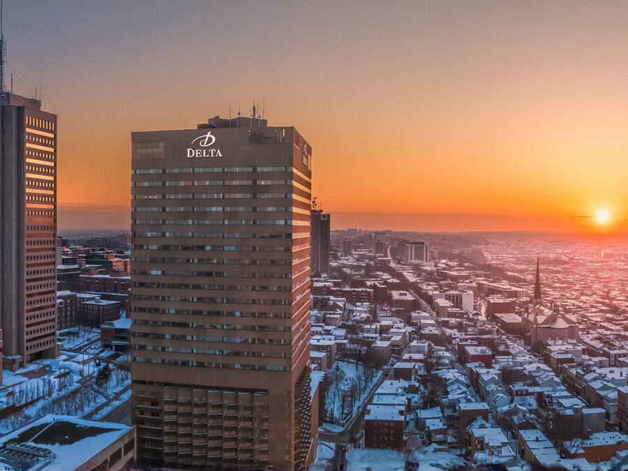 Un edificio alto con el logo de Delta, rodeado por un paisaje urbano con edificios cubiertos de nieve al atardecer.