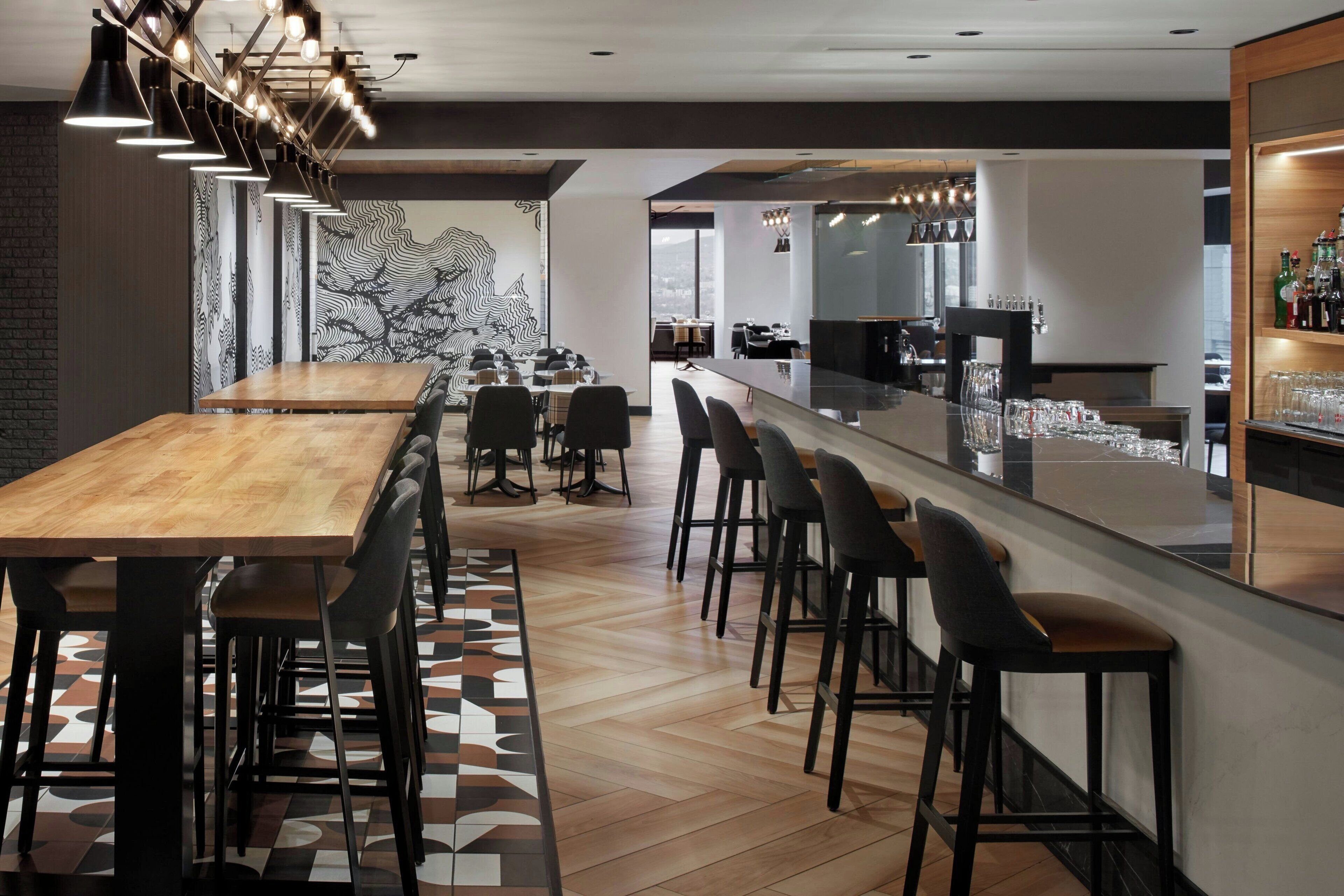 A modern bar area with a long counter, bar stools, and a variety of glasses and bottles.