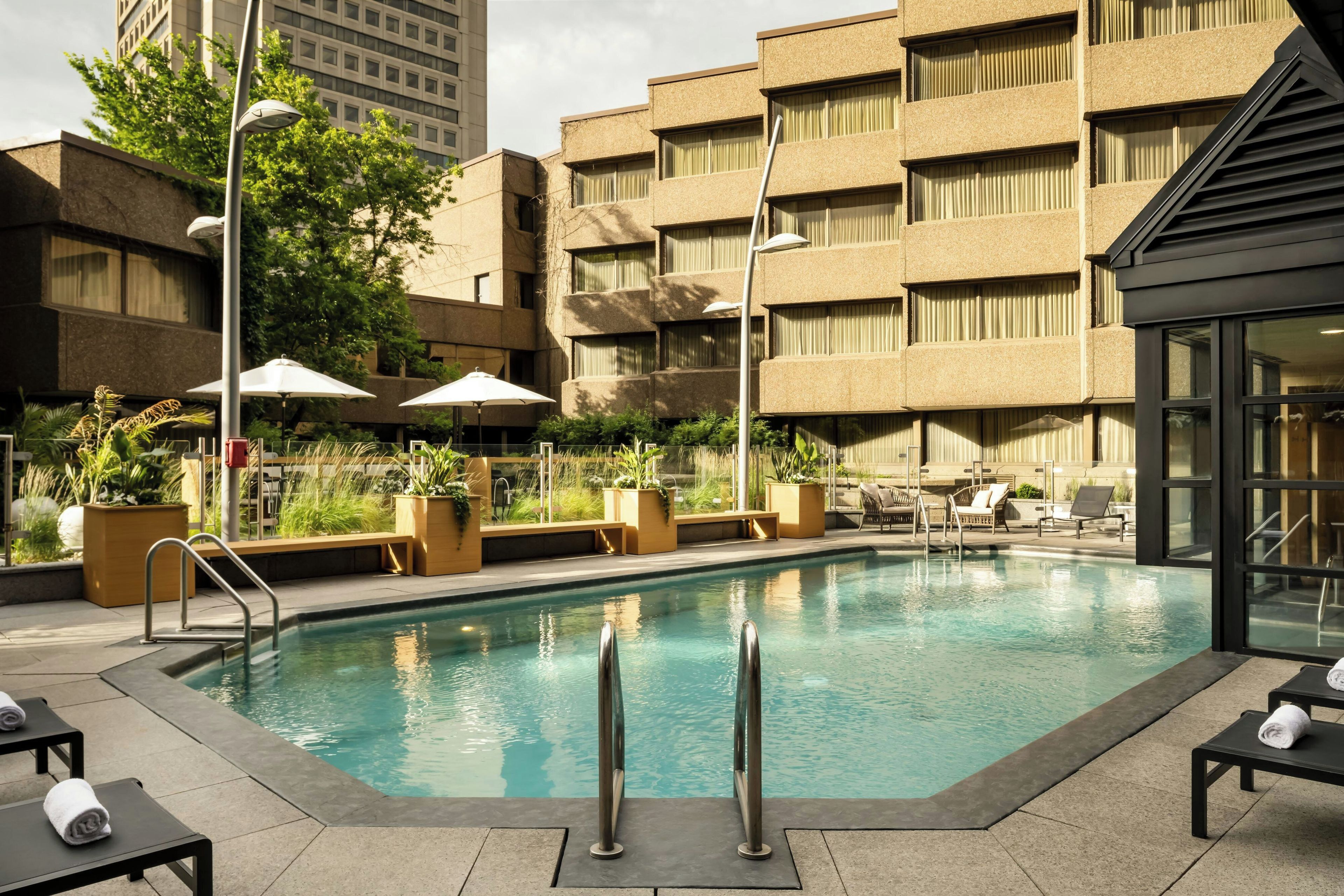 Piscina en la azotea con sillas de descanso y sombrillas, rodeada por un edificio con varios balcones.