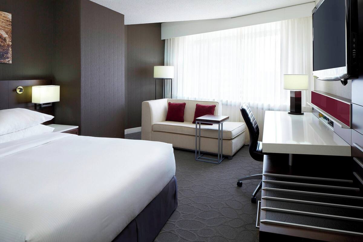 A hotel room with a large bed, a sofa, a desk, and a TV.