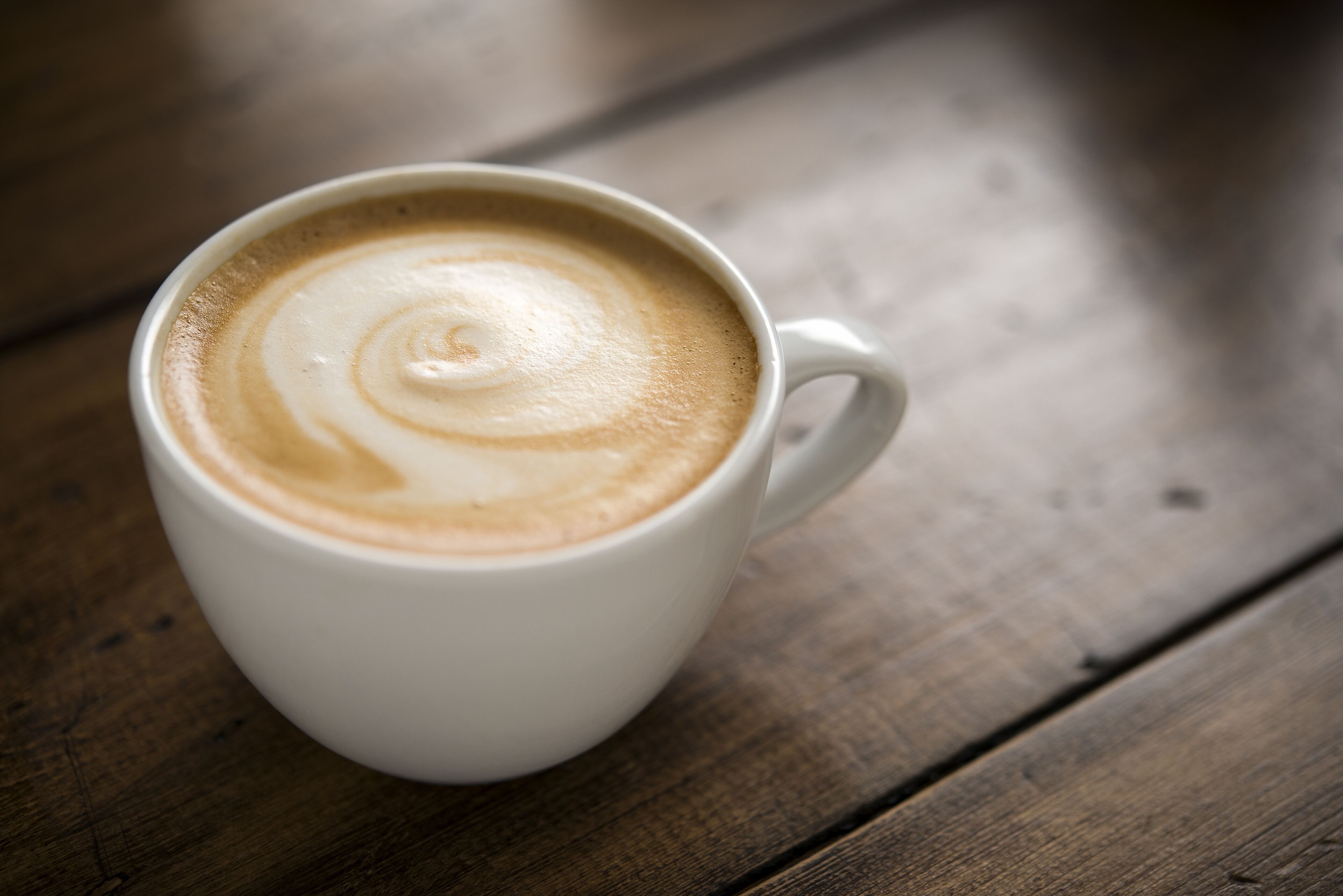 A white cup of coffee with latte art on a wooden surface.