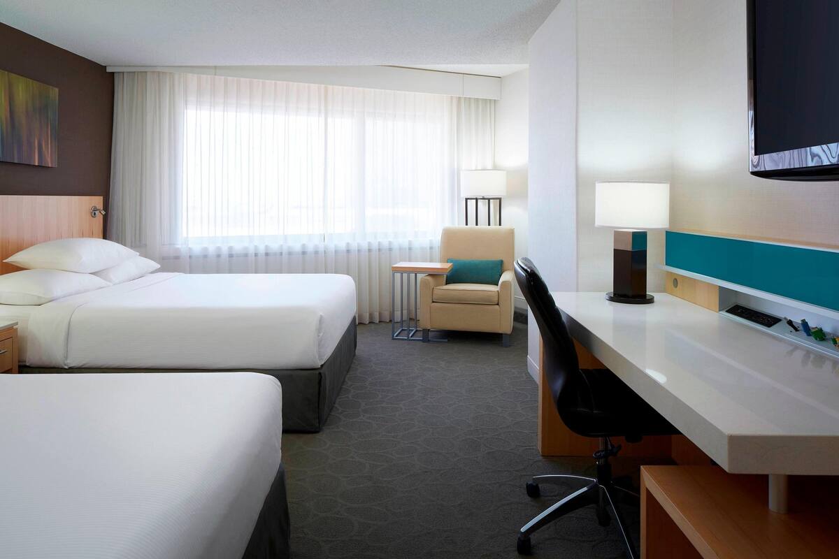 A hotel room with two beds, a desk, a chair, a TV, and a window with curtains.