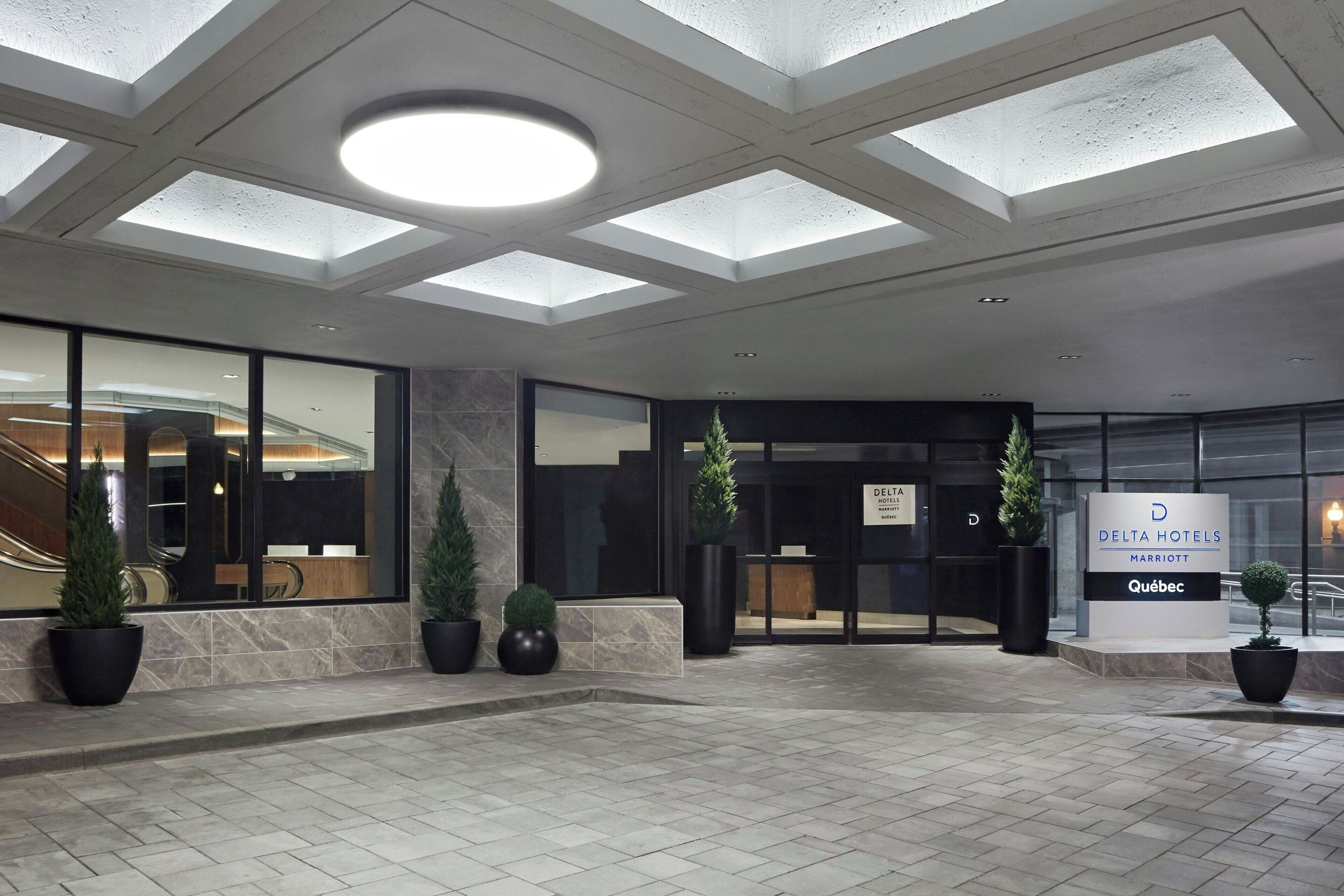 A modern hotel entrance with skylights, a glass facade, and potted plants.