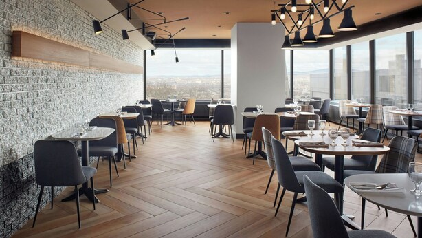 A modern restaurant with a brick wall, wooden flooring, and multiple dining tables and chairs. - Delta Hotels by Marriott Quebec (Québec City)