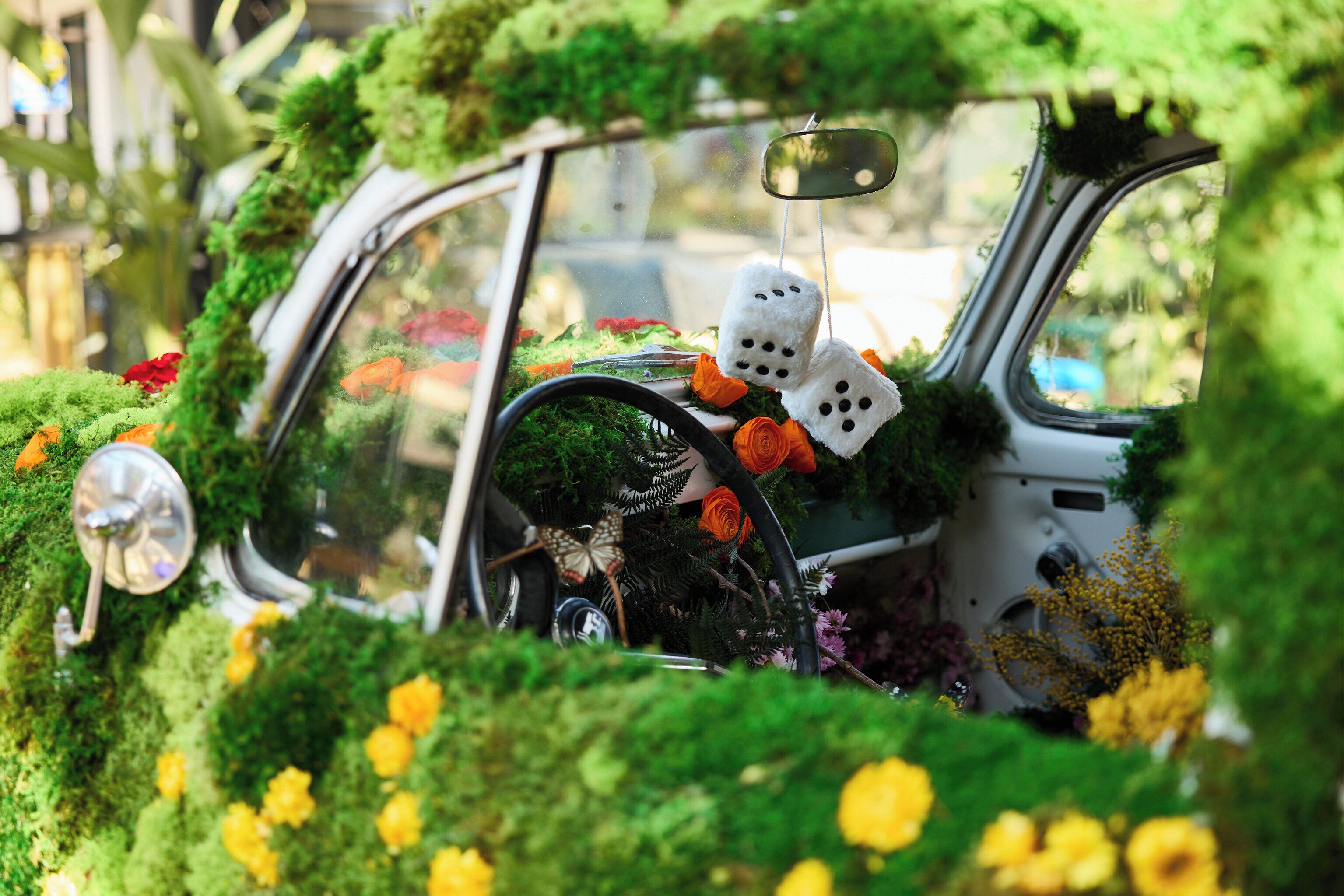 A car covered in greenery and flowers, with dice hanging from the rearview mirror.