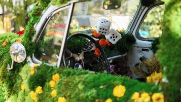 A car covered in greenery and flowers, with dice hanging from the rearview mirror.
