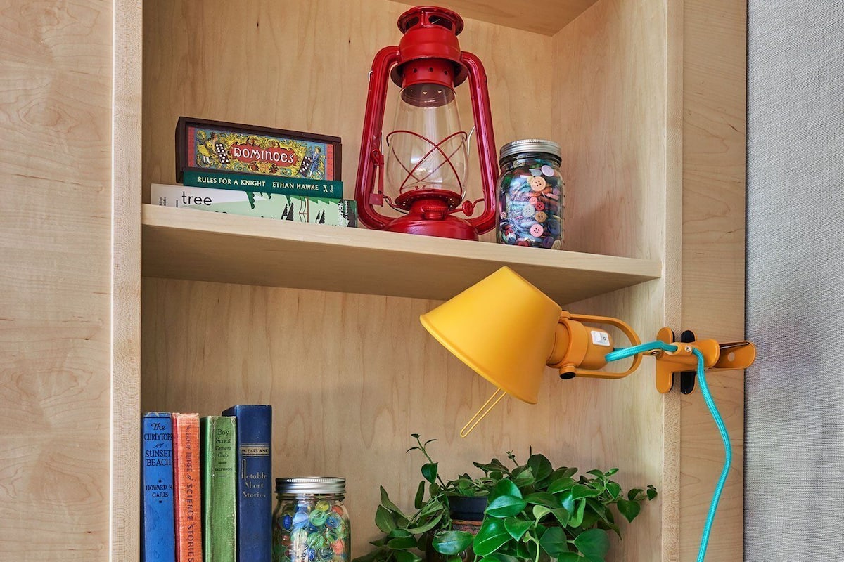 A wooden bookshelf with books, a lantern, a jar of candies, and a potted plant.