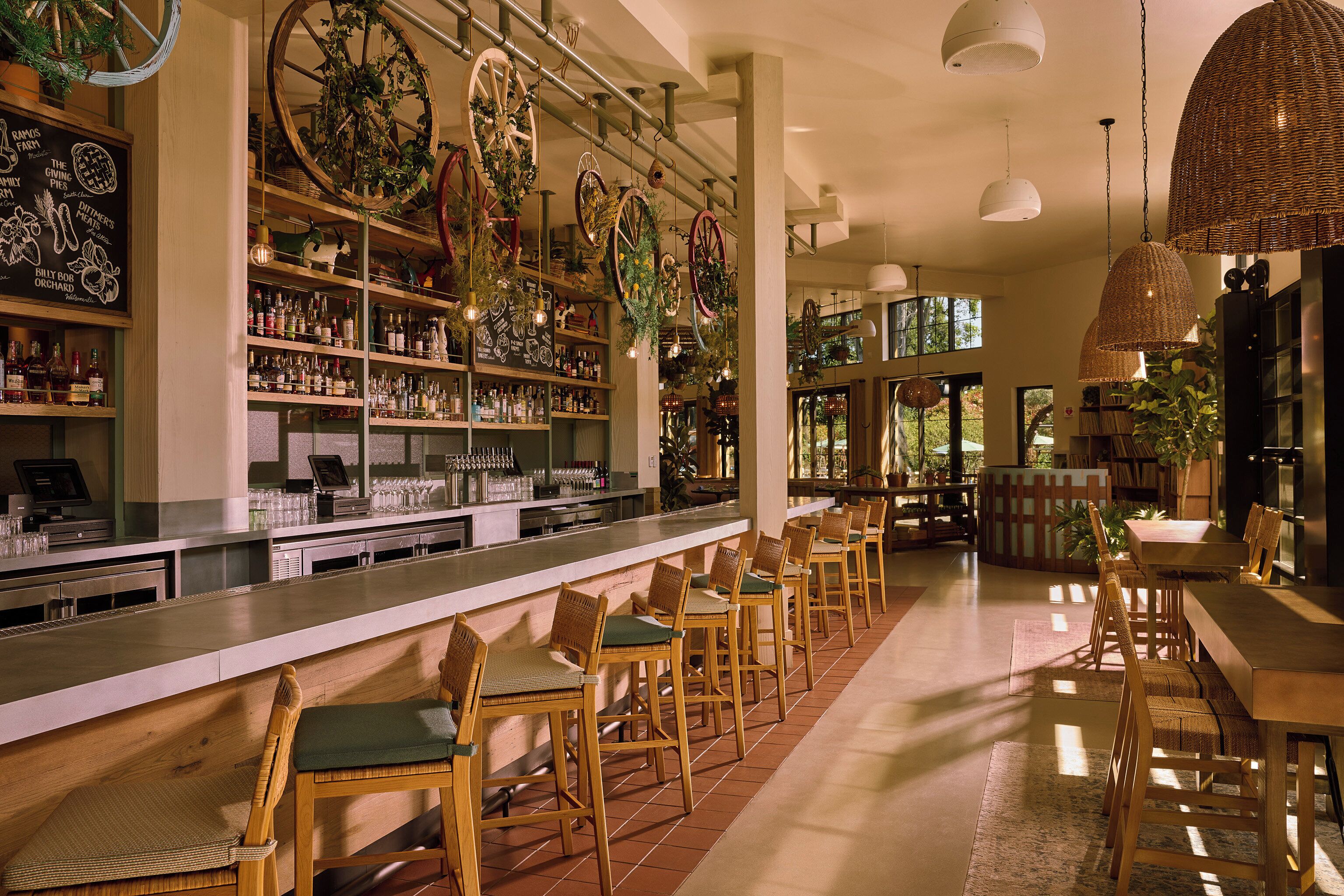 A bar area with wooden chairs, shelves with bottles, and hanging decorations.