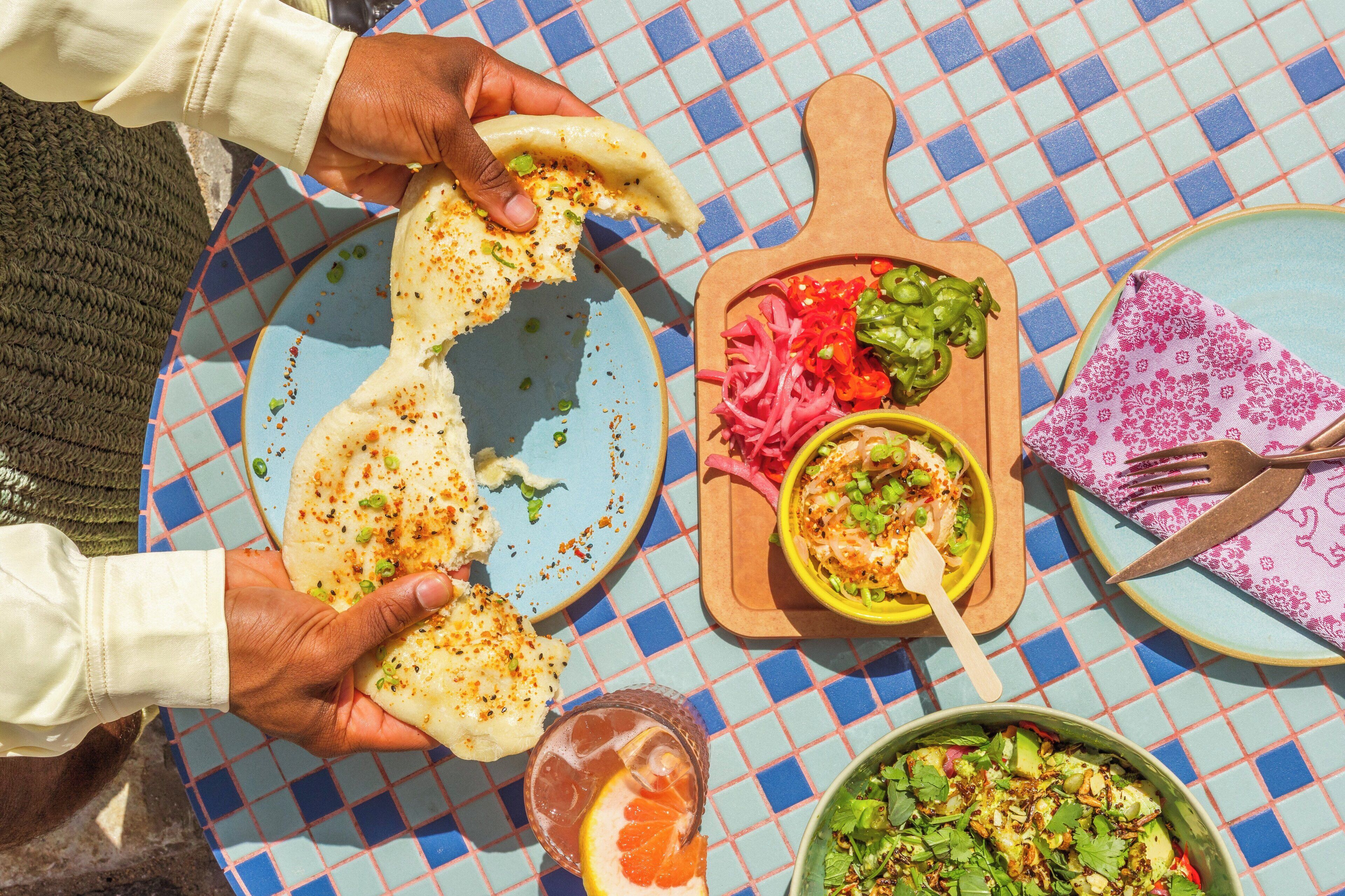 A table with a checkered tablecloth, a plate with flatbread, a bowl of salad, and a glass of drink.