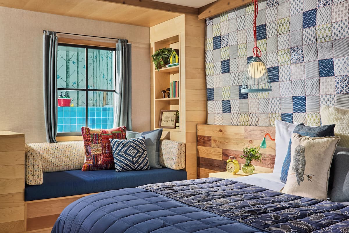 A cozy bedroom with a built-in bench, a large bed, a wooden headboard, a quilted bedspread, and a patchwork wall.