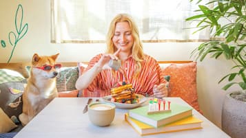 A person sitting at a table with a dog, pancakes, a book, and a cup.