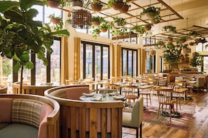 Un restaurant spacieux, doté de meubles en bois, de grandes fenêtres et de plantes suspendues.