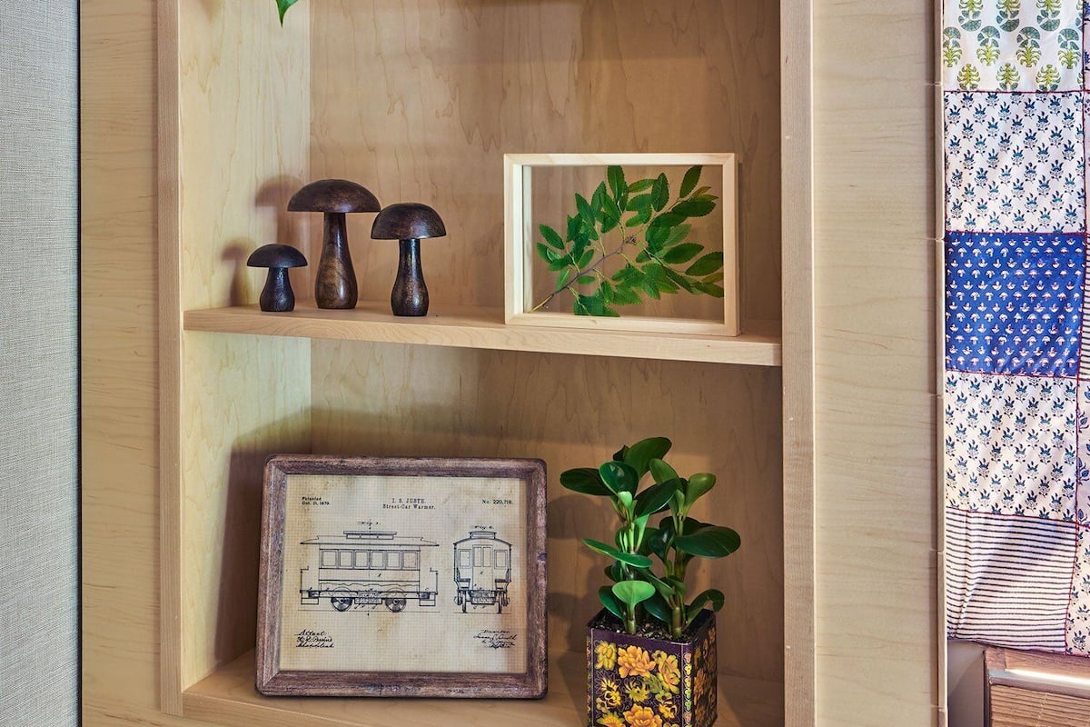 A wooden shelf with a house-shaped decoration, a framed leaf, and a framed blueprint.