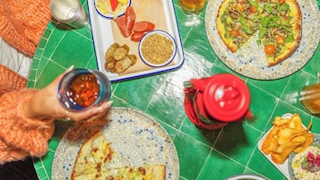 Una mesa de comedor con diversos platos, entre ellos pizzas y una bandeja con salchichas y verduras.