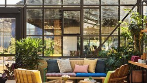 A modern interior with a large glass window, a wooden sofa, and various plants. - Treehouse Hotel Silicon Valley (Sunnyvale)