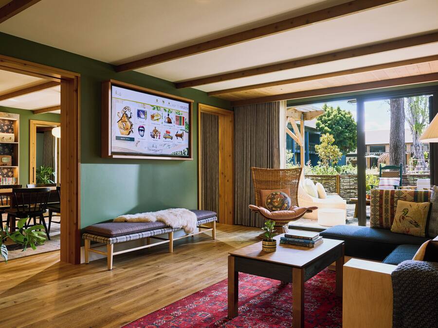 A cozy living room with a wooden bench, a sofa, a table, and a large window offering a view of the outdoors.