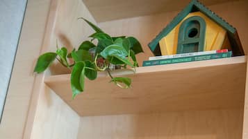 Uma prateleira de madeira com um vaso em forma de casa, uma folha emoldurada e uma planta baixa emoldurada.