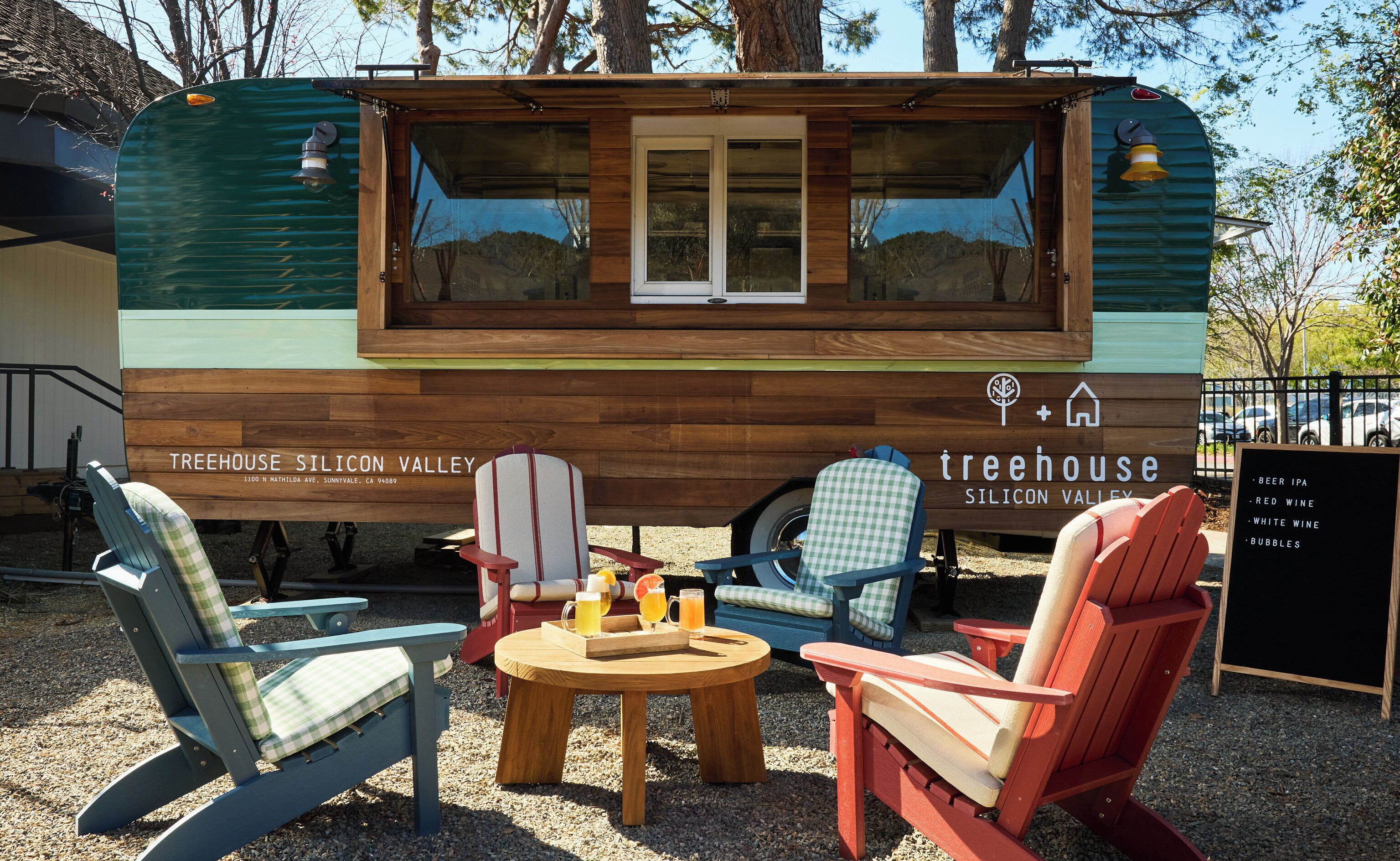 A Treehouse Silicon Valley food truck with a wooden exterior, seating area with chairs and a table, and a menu board listing beverages.