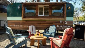A Treehouse Silicon Valley food truck with a wooden exterior, seating area with chairs and a table, and a menu board listing beverages.