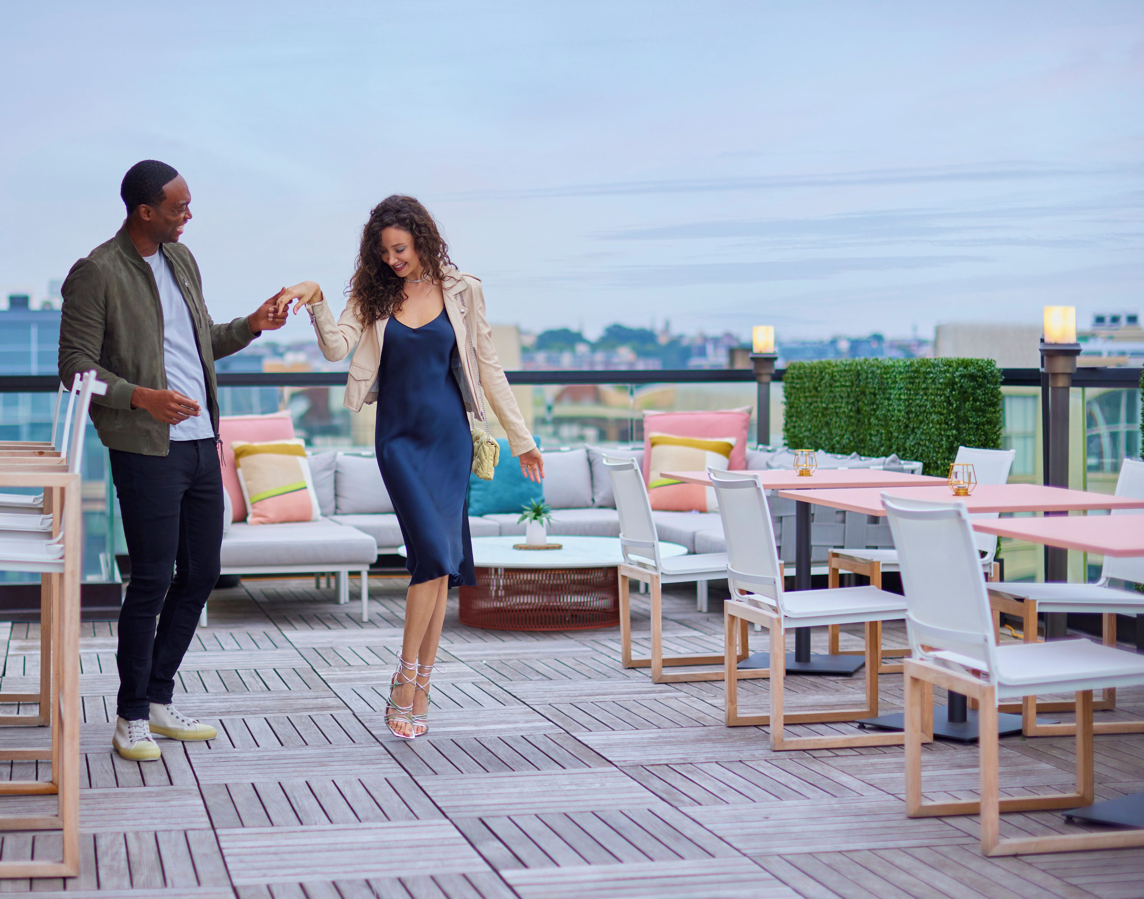 A couple on a rooftop terrace with outdoor seating and a city view.
