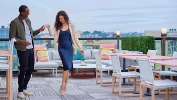 A couple on a rooftop terrace with outdoor seating and a city view.