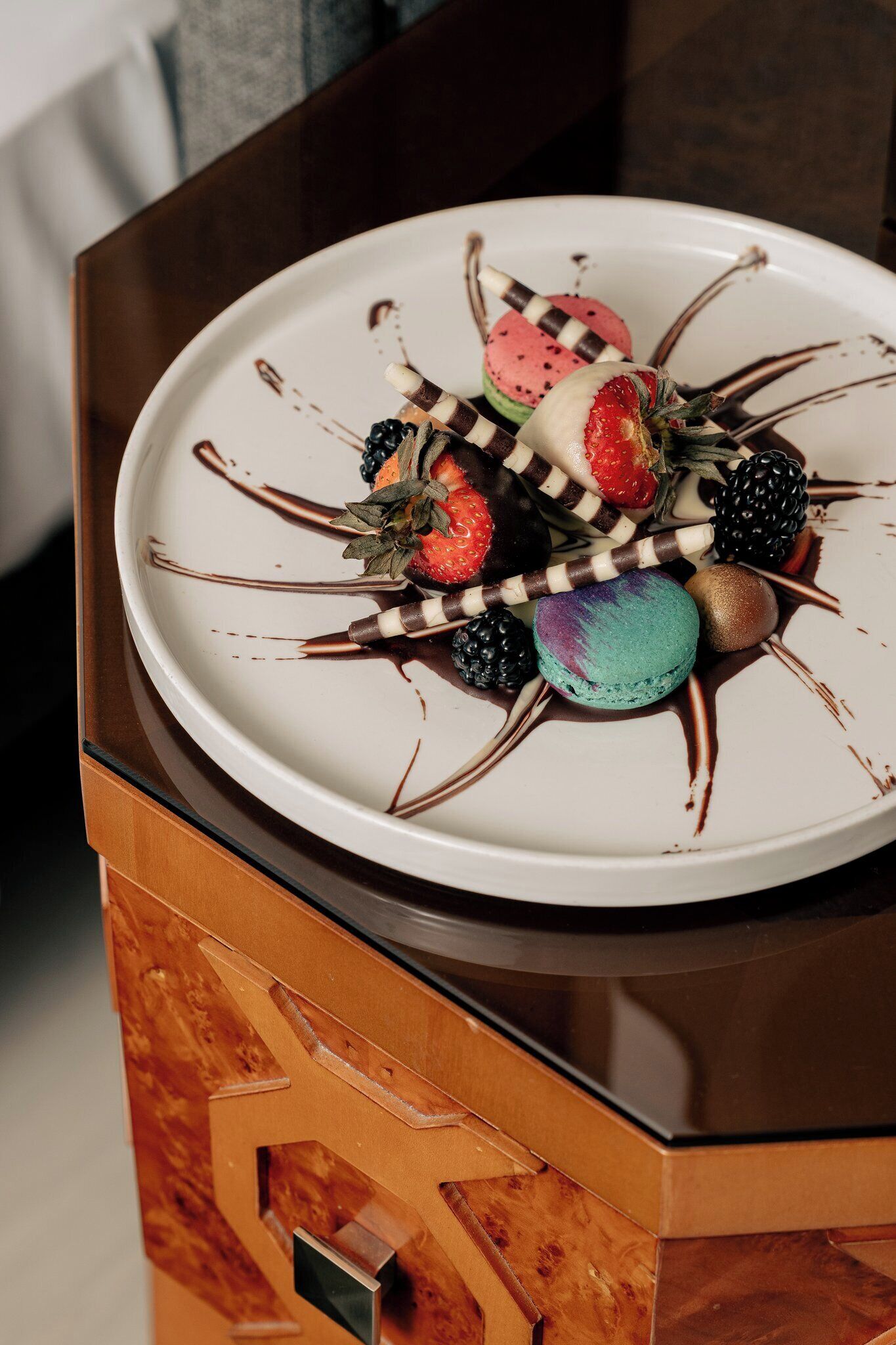 A dessert plate with various fruits and macarons on a white plate, placed on a wooden cabinet.